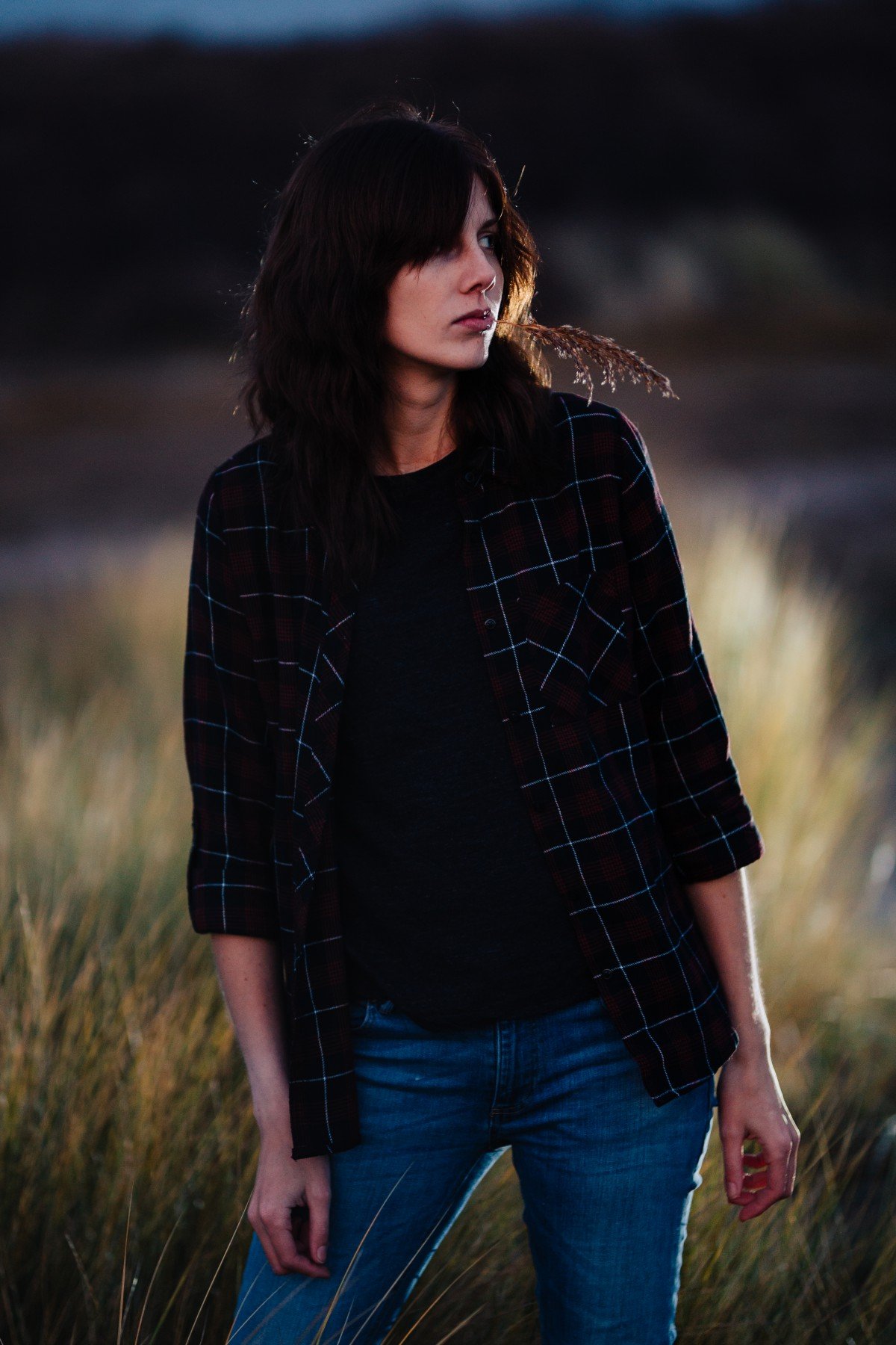A woman in jeans and a checked shirt standing in a field, captured through the lens of a Sigma art 85 mm 1.4.