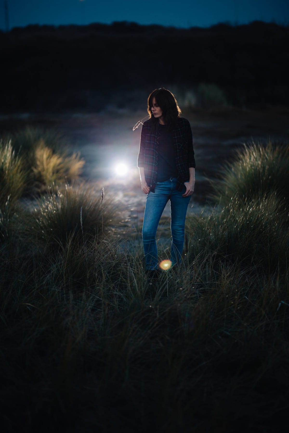 Een vrouw die 's nachts in een veld staat en een Sigma art 85 mm 1.4 lens gebruikt om haar omgeving te verlichten met een zaklamp.