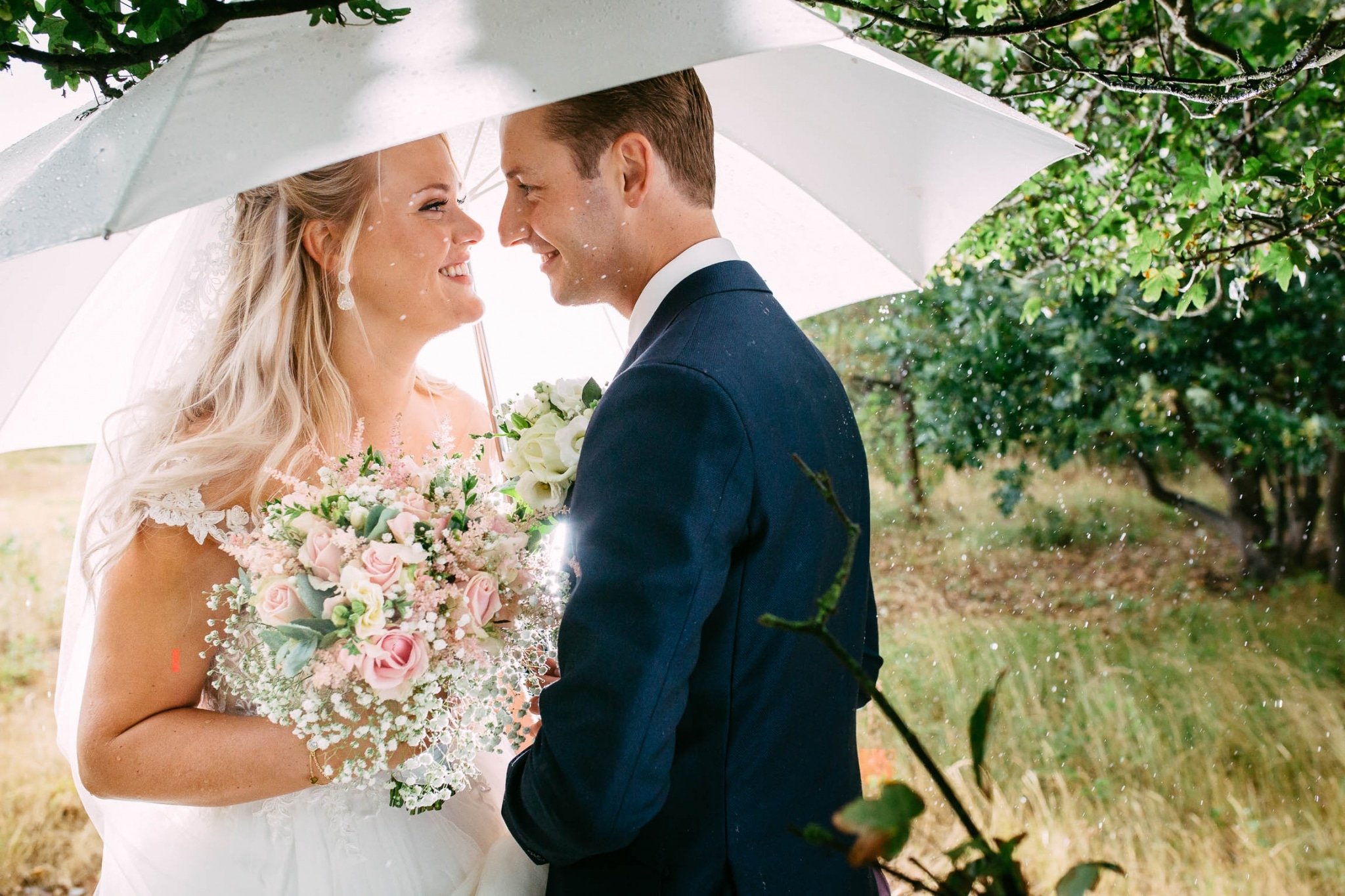 A bride and groom stand under an umbrella.