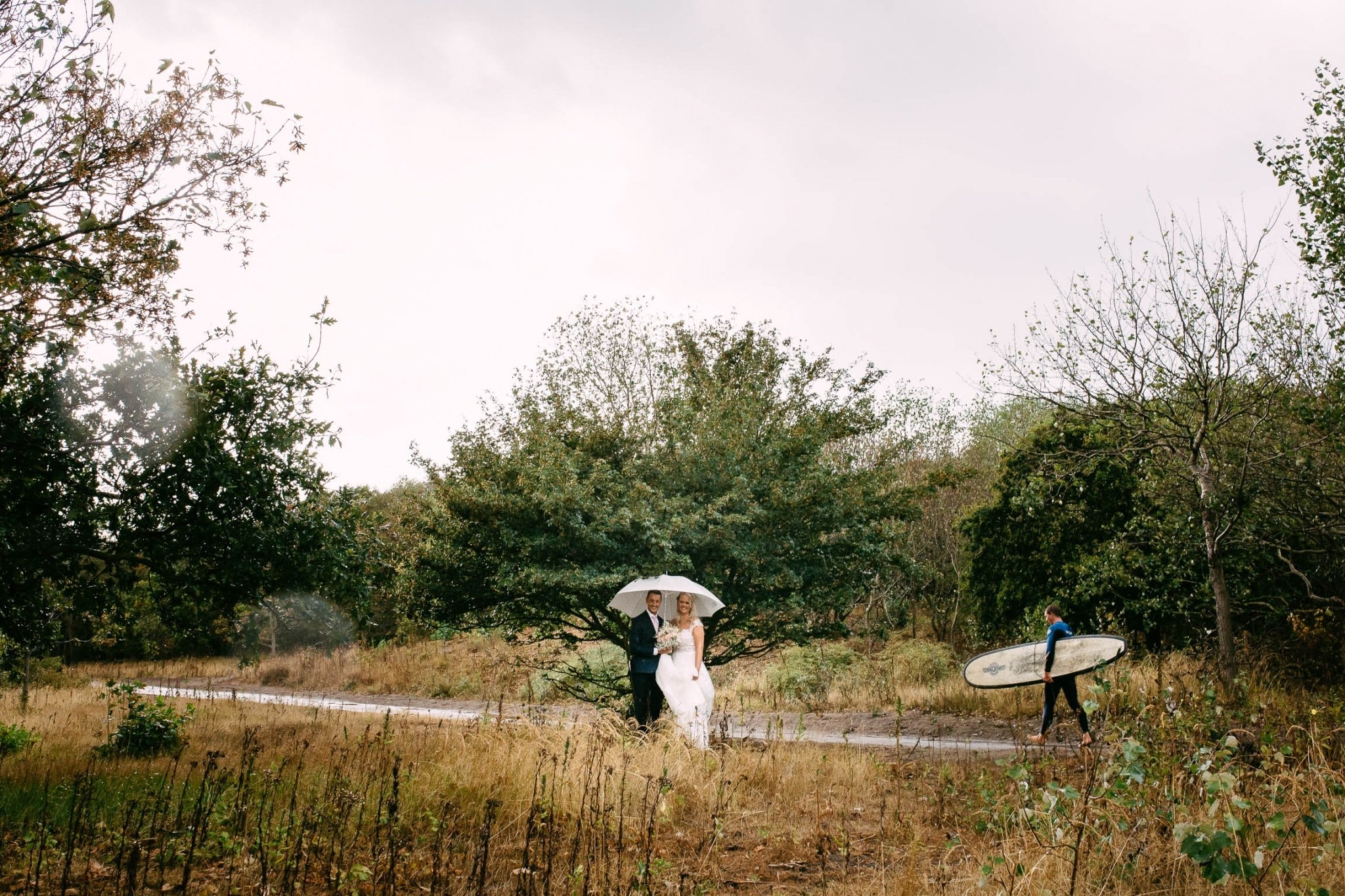 A bride and groom walk down a path with an umbrella.