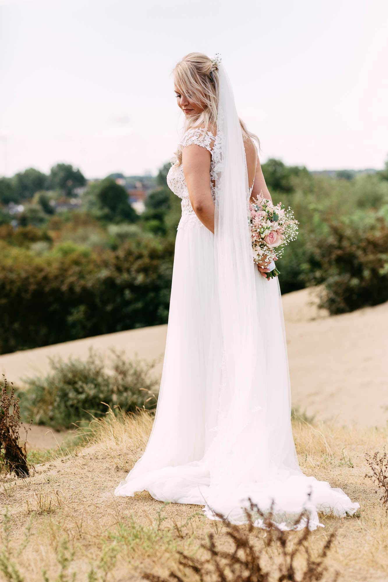 A bride in a white wedding dress standing in a sand dune.