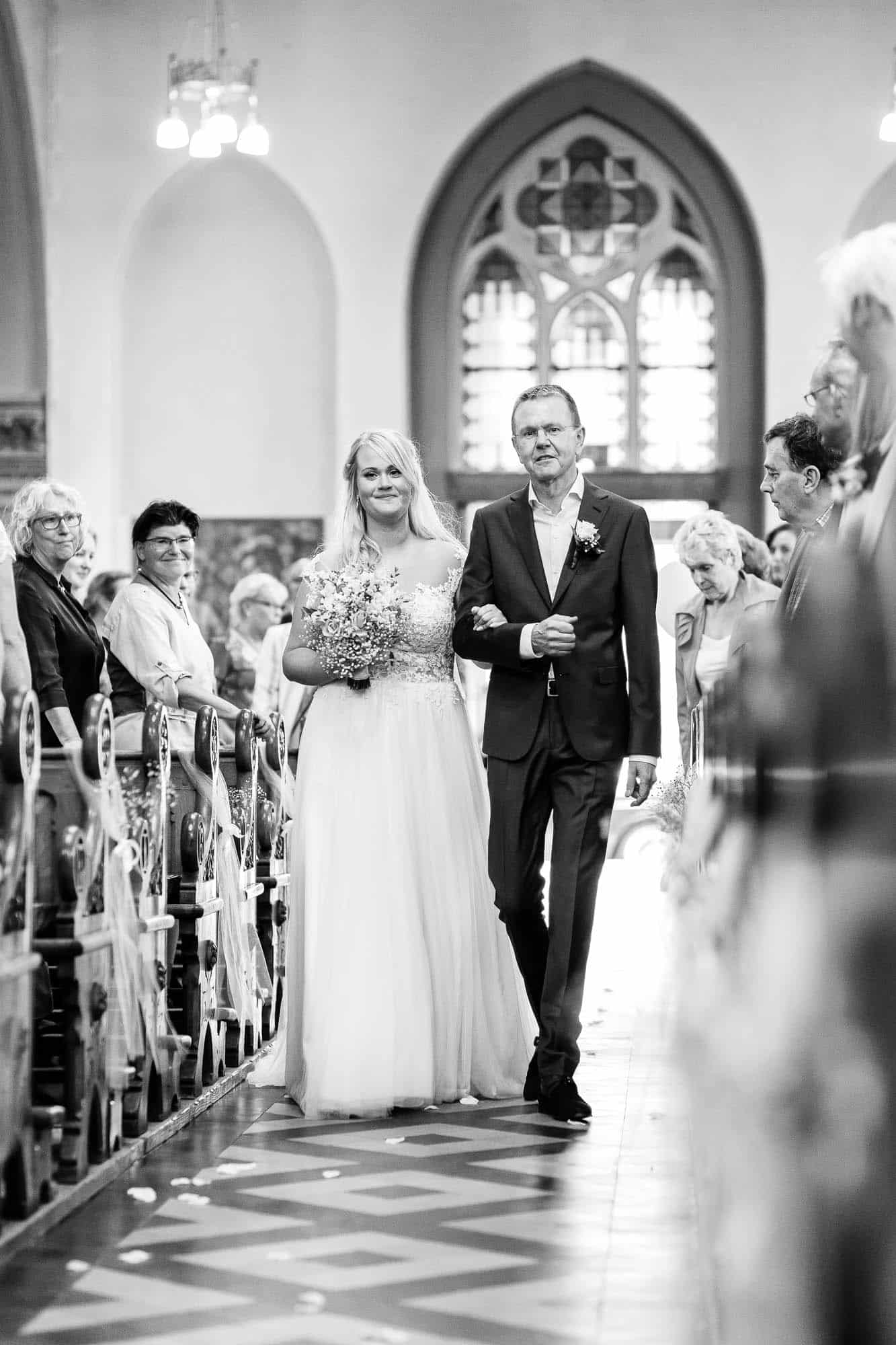 A bride and groom walk down the aisle of a church.