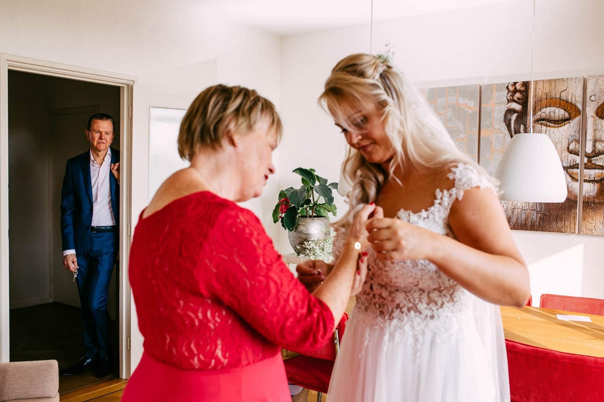 A bride helps her mother put on her wedding dress.