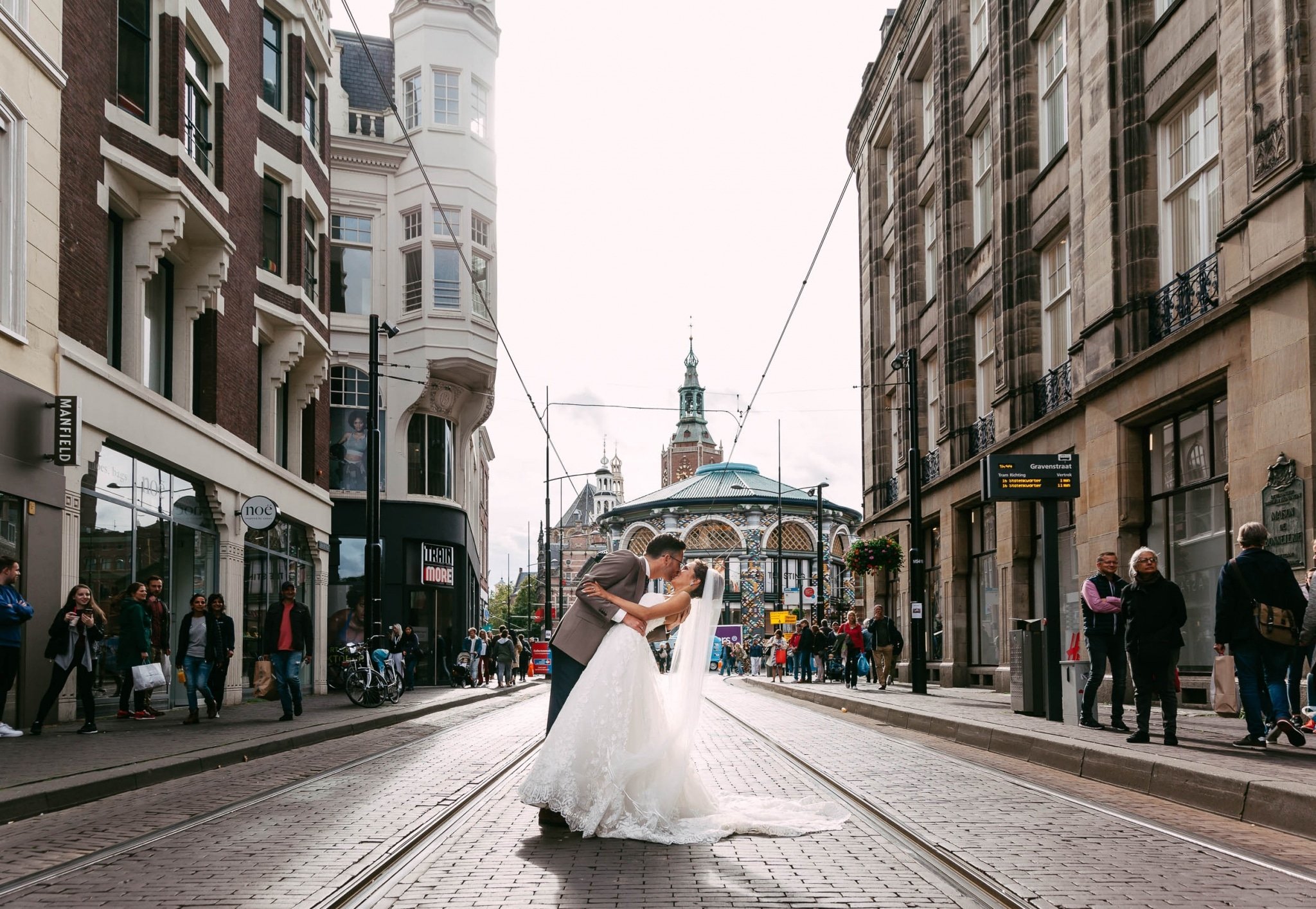 Een bruid en bruidegom kussen op straat in Amsterdam.