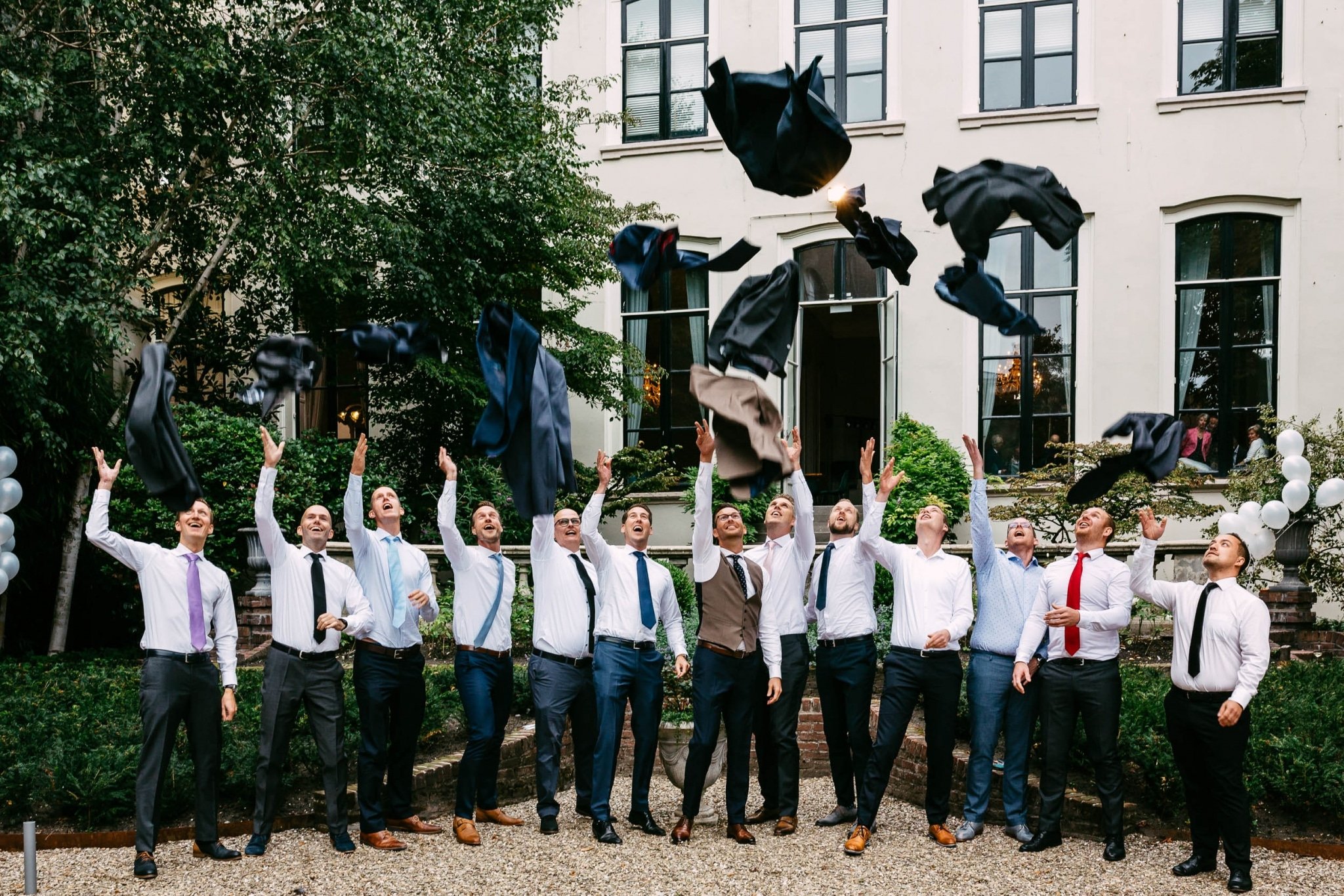 Een groep bruidsjonkers gooit hun stropdassen in de lucht.
