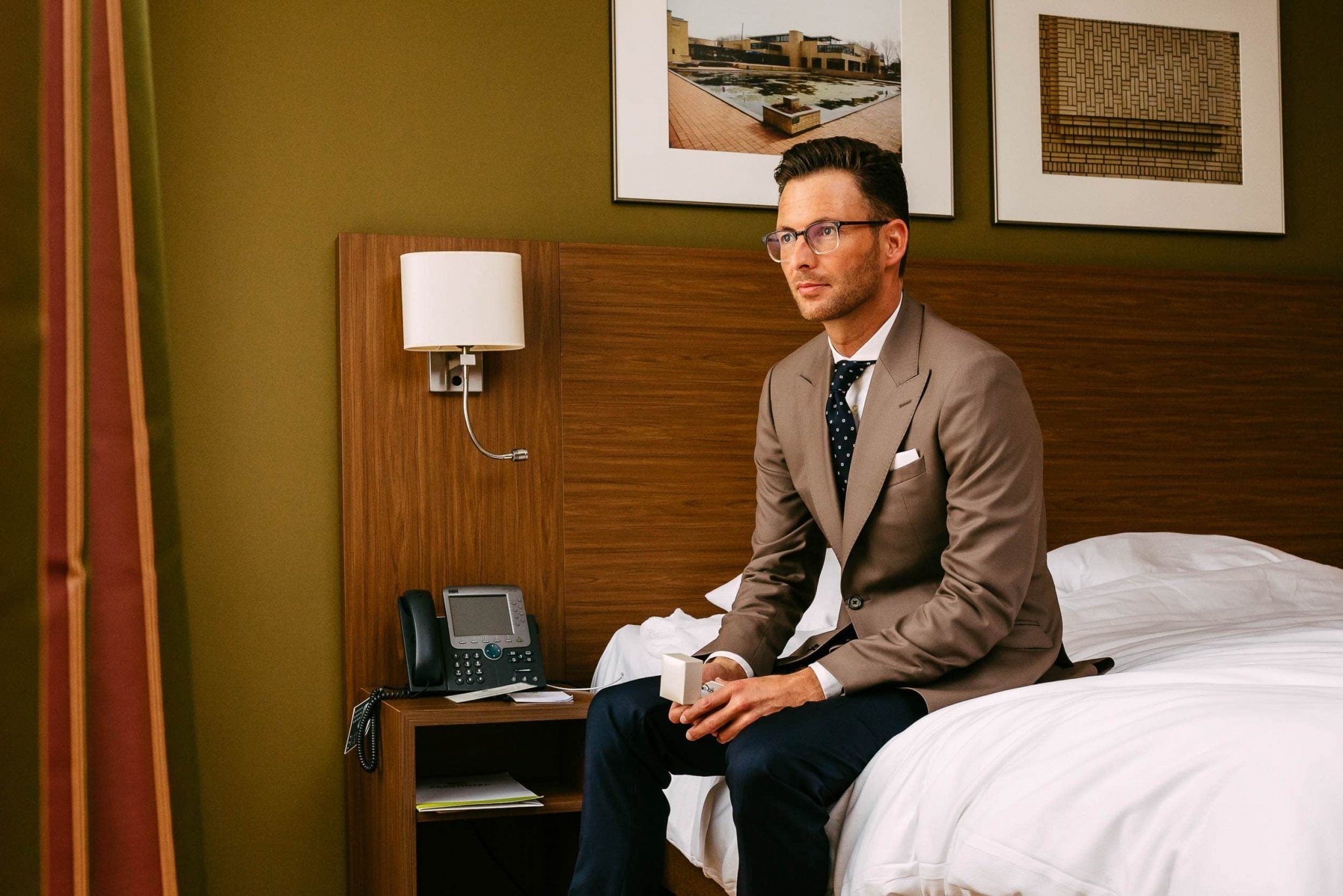 Een man zit op een bed in een hotelkamer.