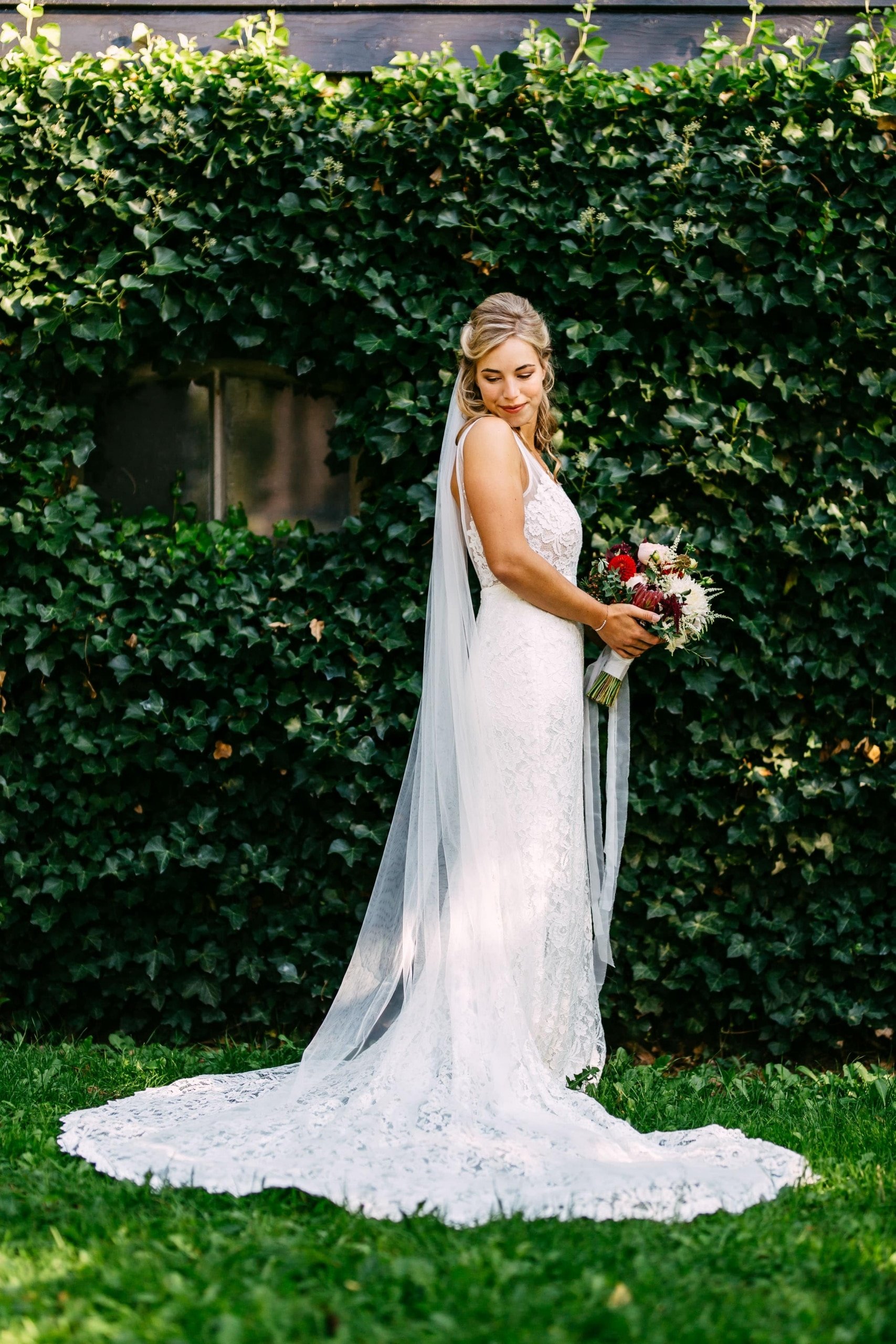 A bride poses in front of an ivy-covered wall.