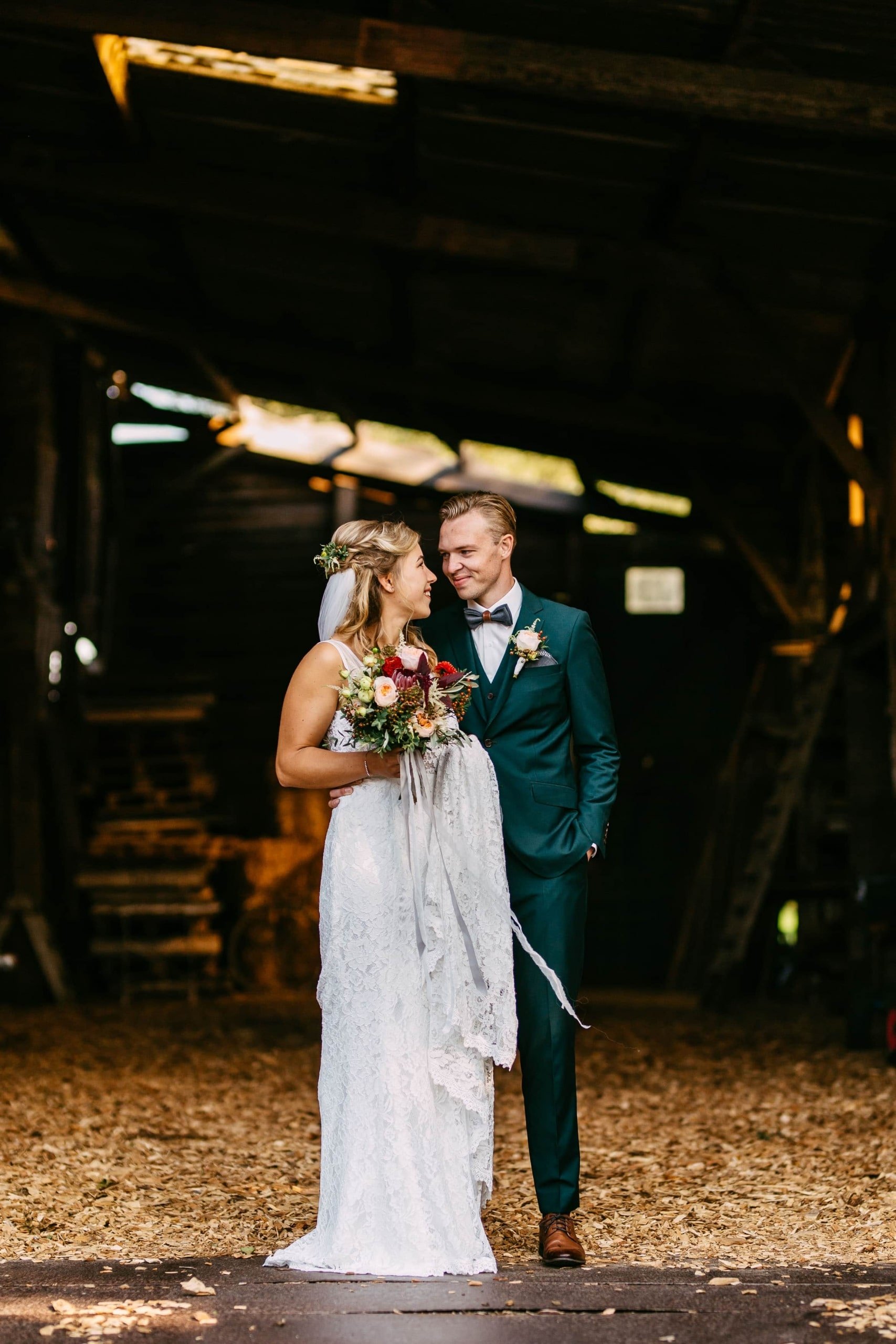 A bride and groom stand in a barn.