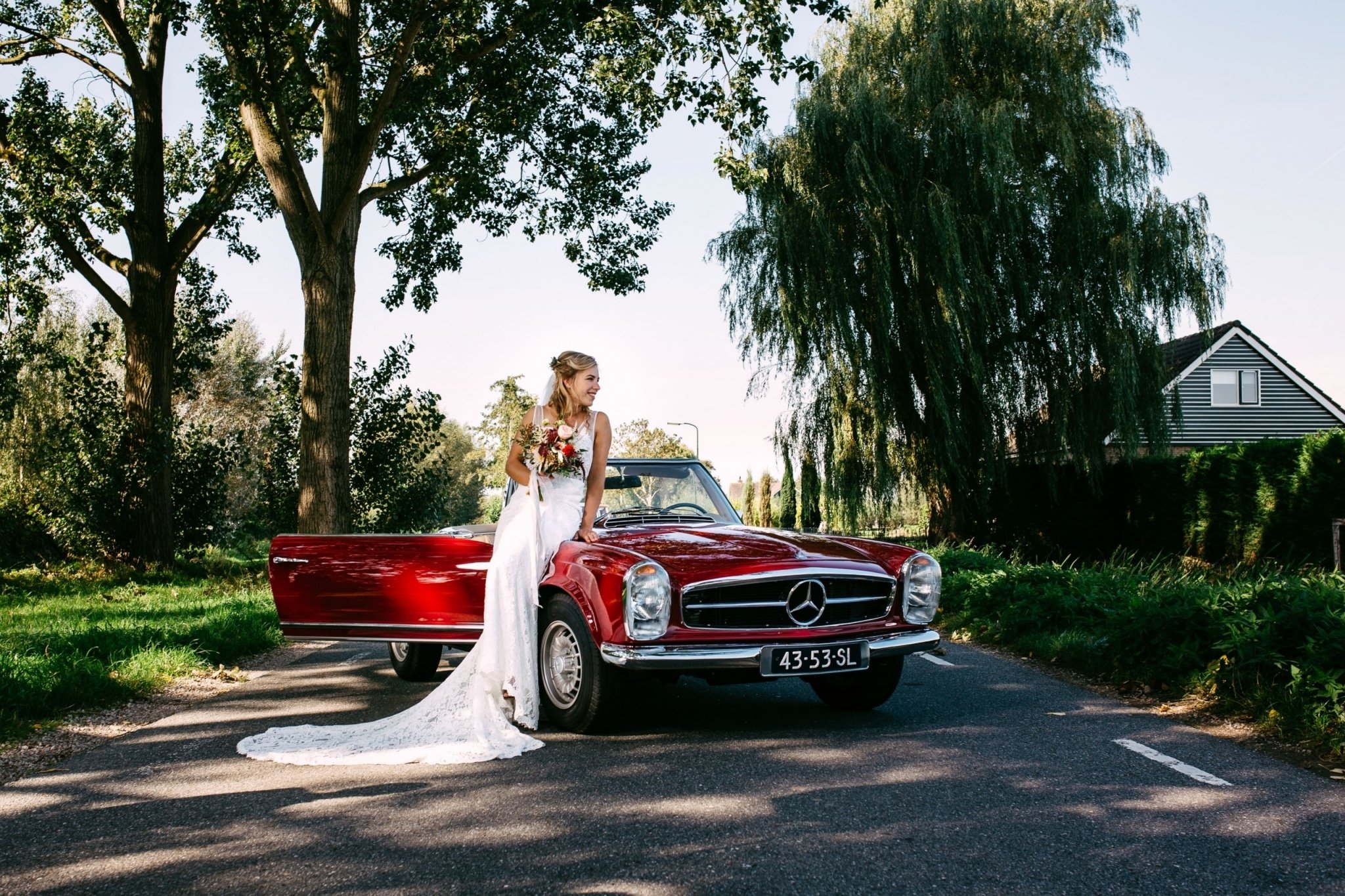 Een bruid in een trouwjurk staat naast een vintage Mercedes-Benz.