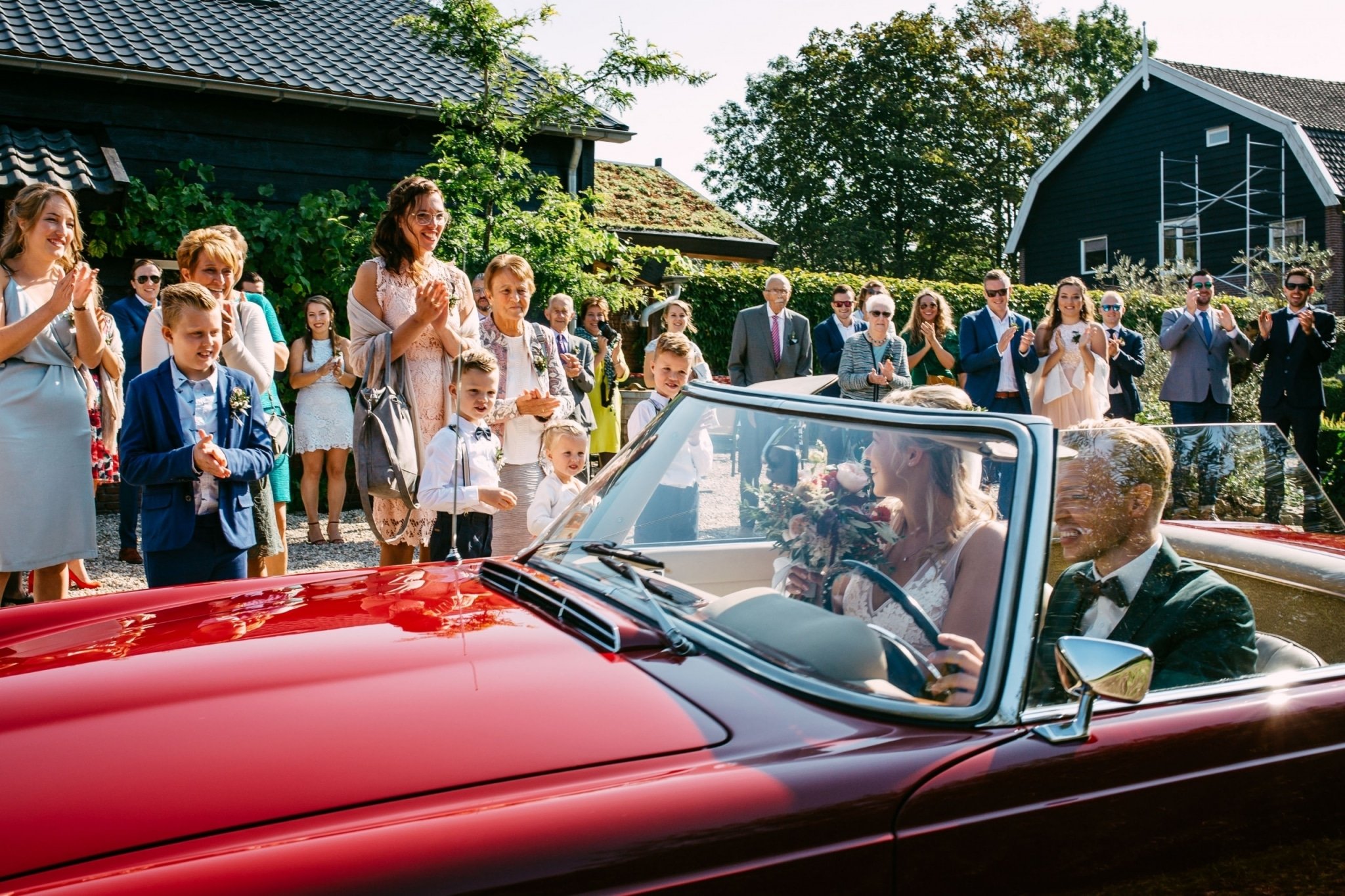 A bride and groom in a red convertible wedding car.