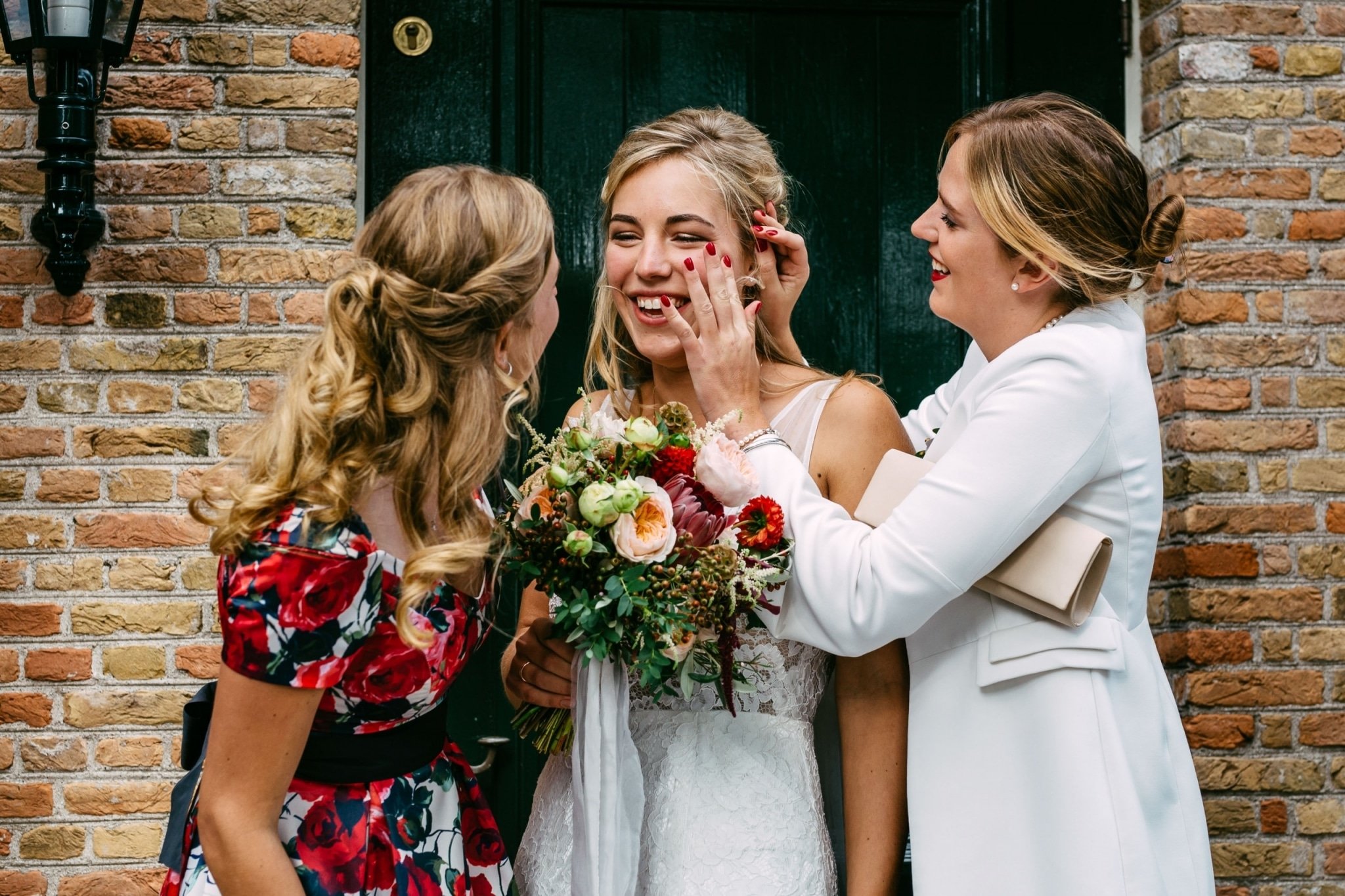 Een bruid en haar bruidsmeisjes kussen elkaar voor een bakstenen deur.