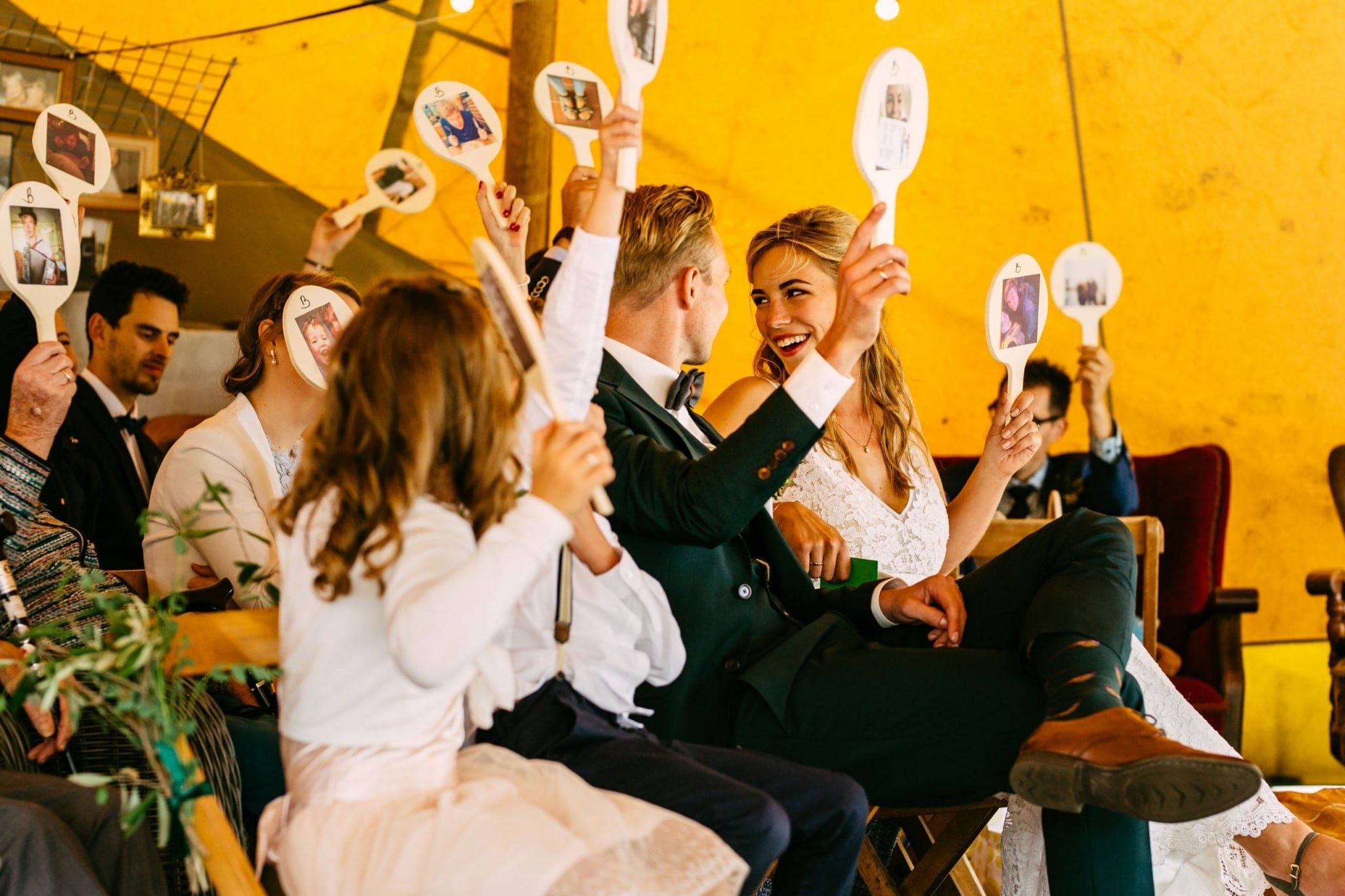 Een huwelijksceremonie in een tent met mensen die foto's omhoog houden.