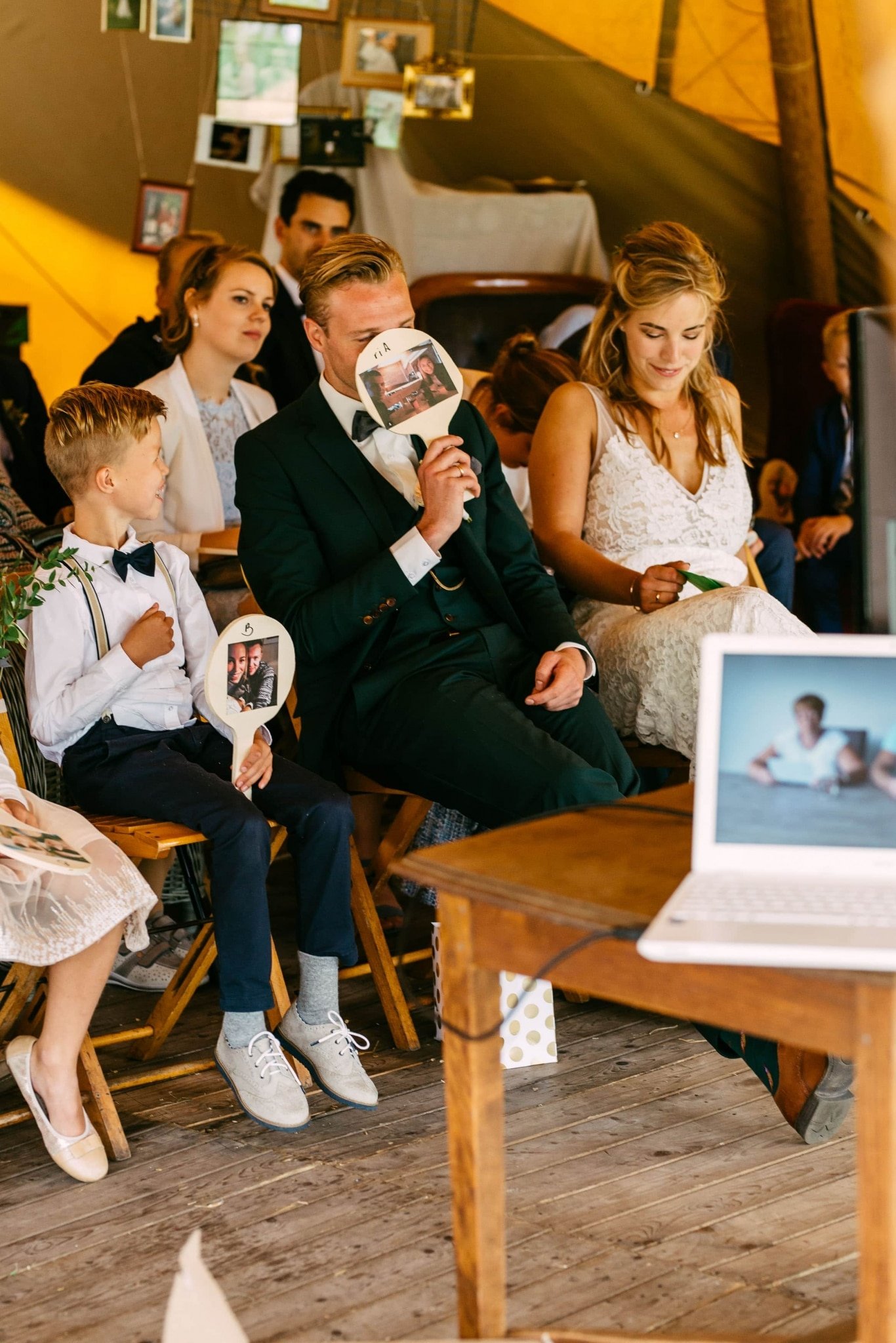 A group of people sit in a tent with a laptop in front of them.