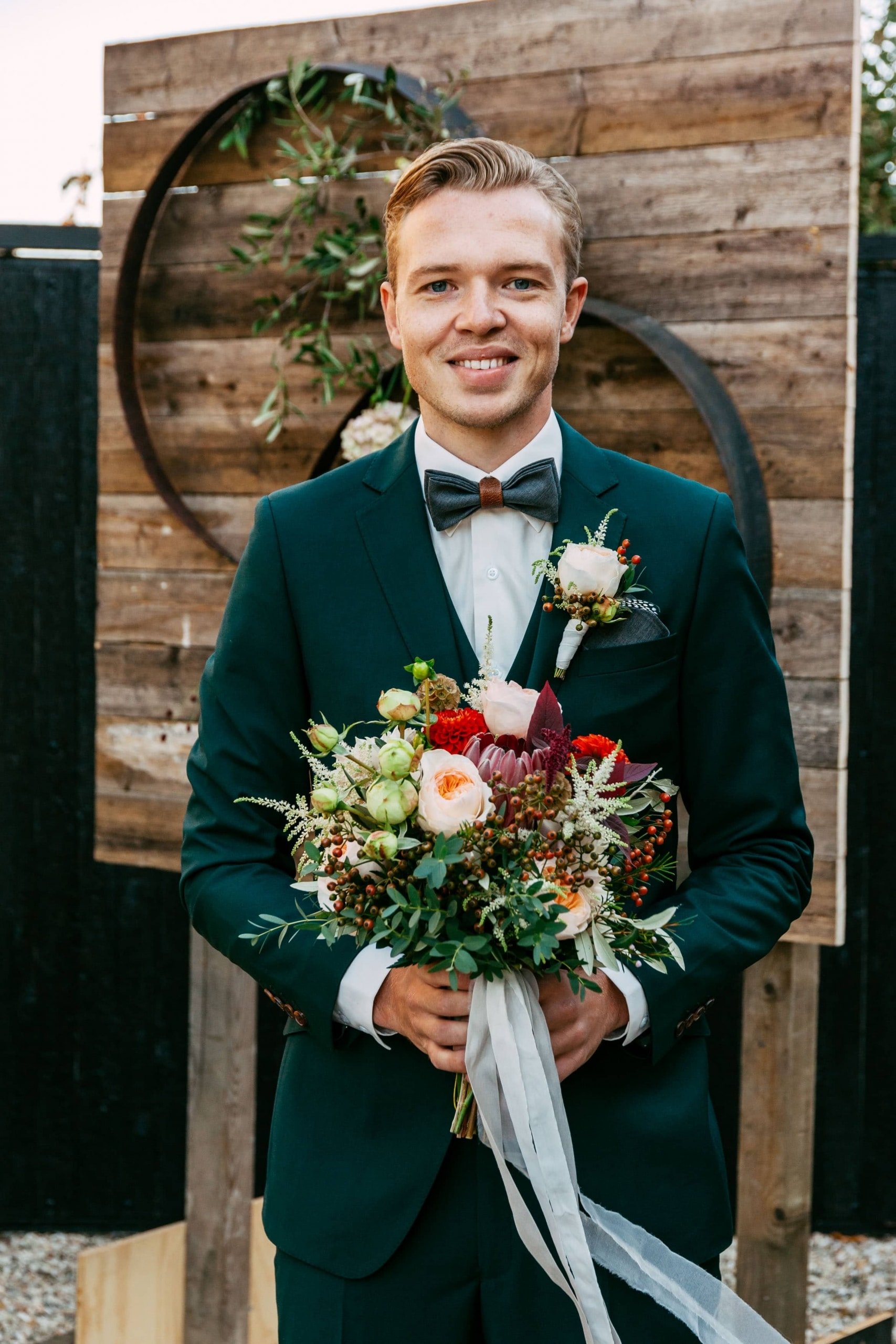 A groom in a green suit with a bouquet.