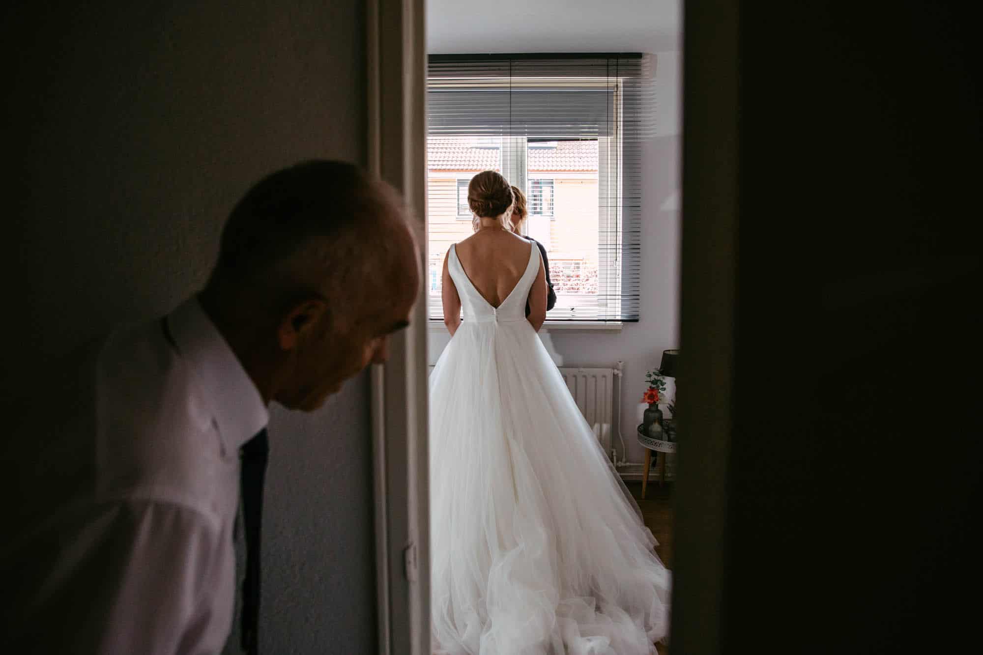 A bride stands in front of a mirror and looks at her wedding dress.