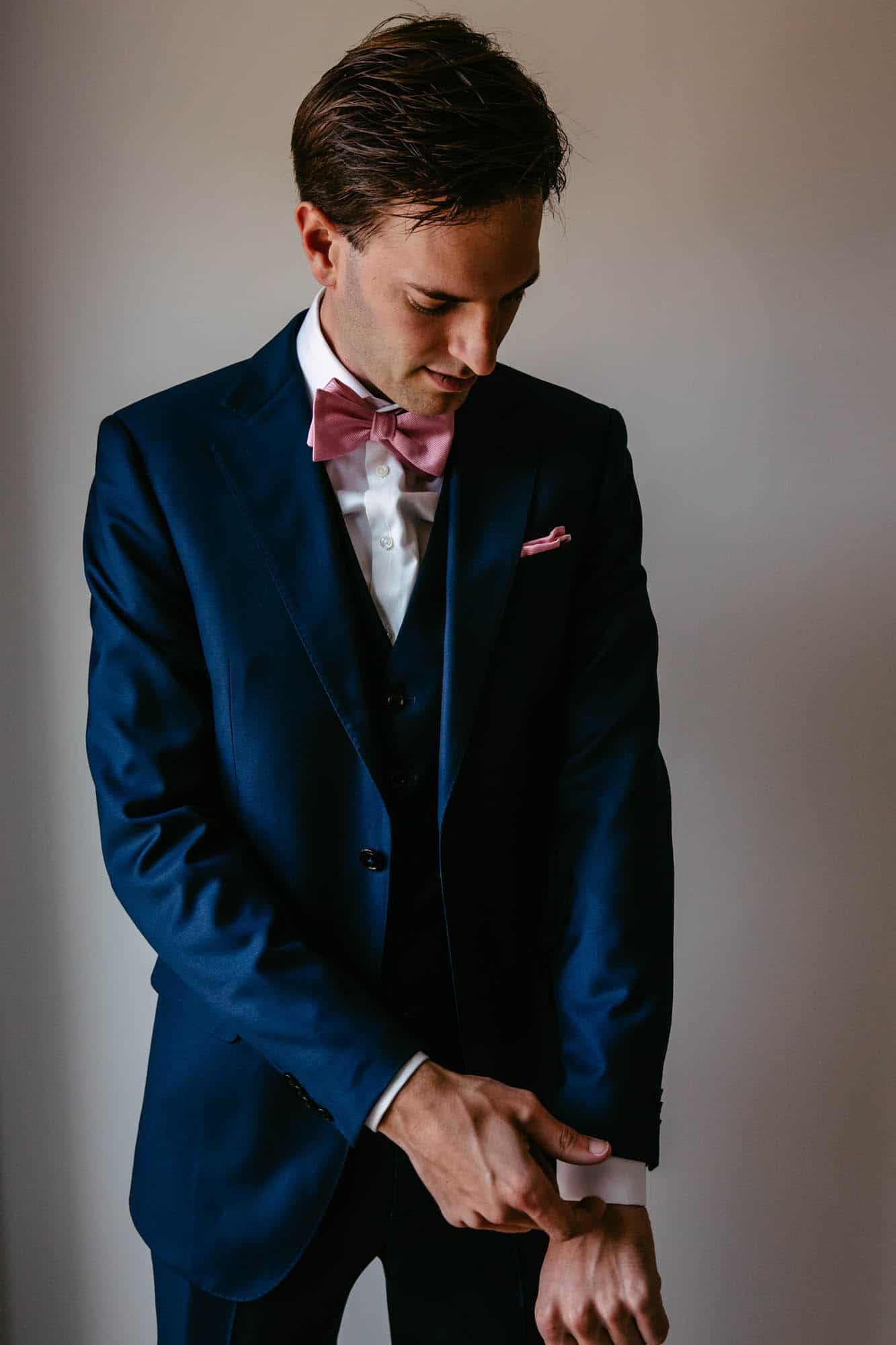 A man in a blue suit with a pink bow tie.