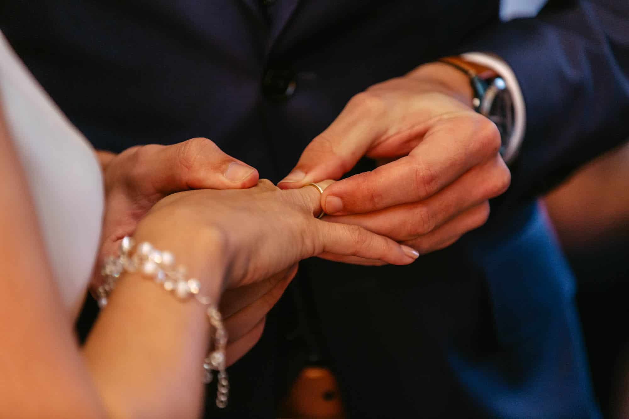 A man puts a wedding ring on a bride's hand.
