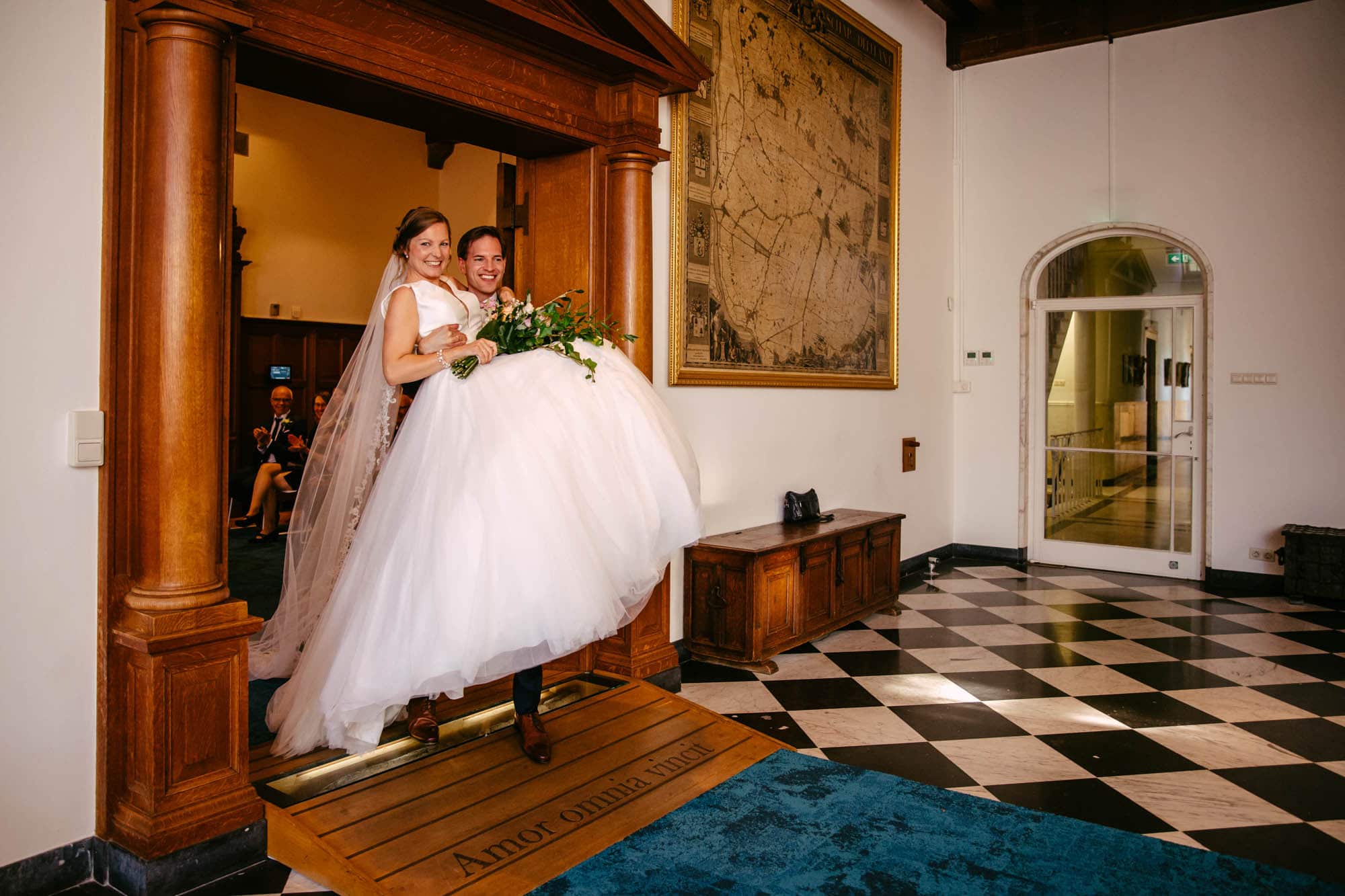 A bride carries her wedding dress into a room.