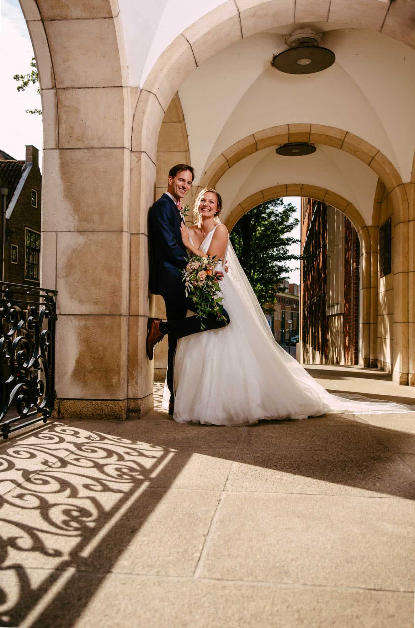 A bride and groom pose under an archway.