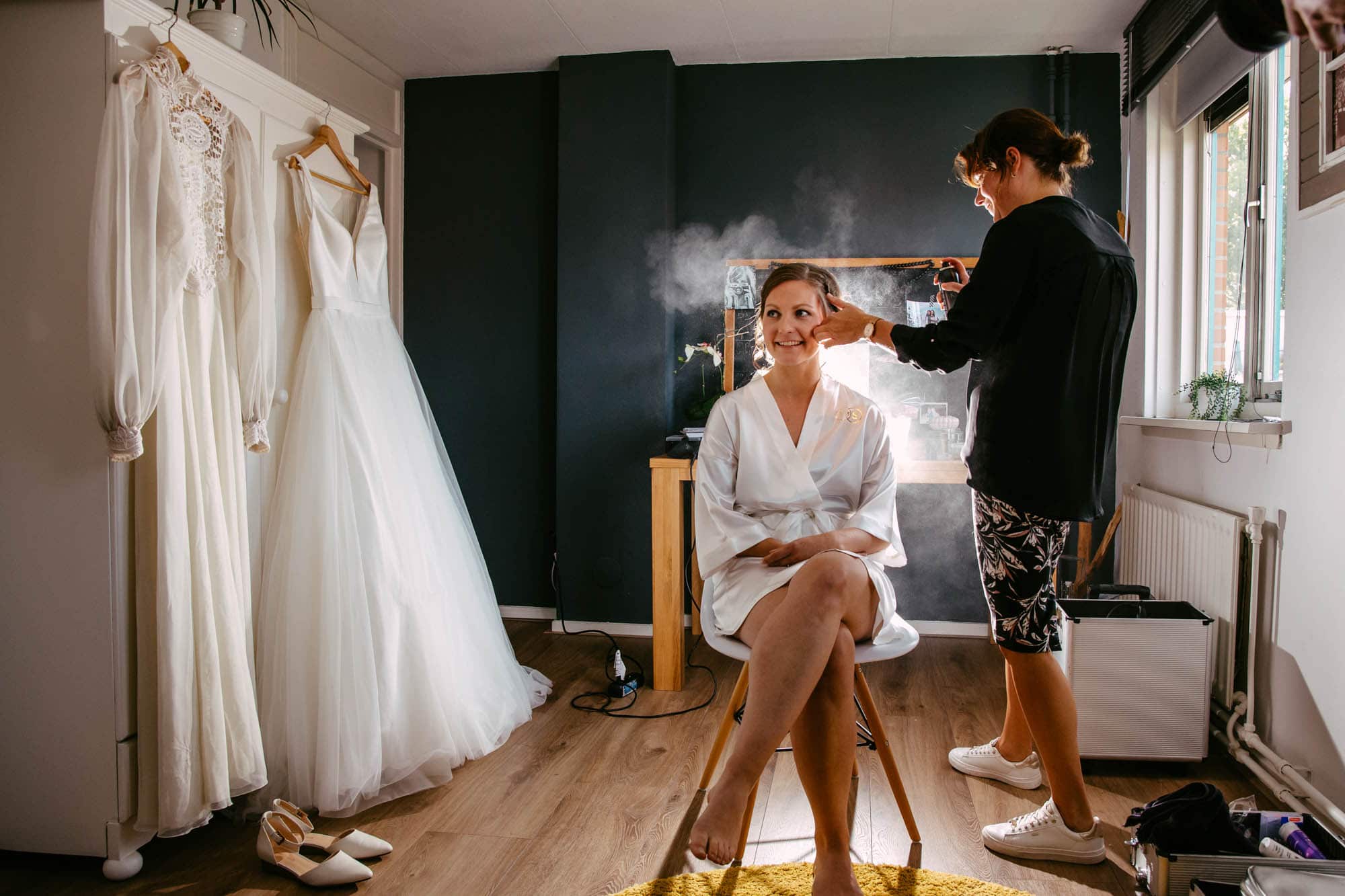 A bride having her hair and make-up done in a room.