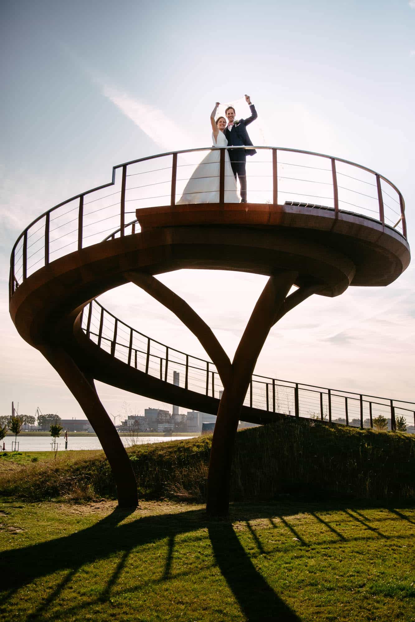 A bride and groom stand on a wooden bridge.