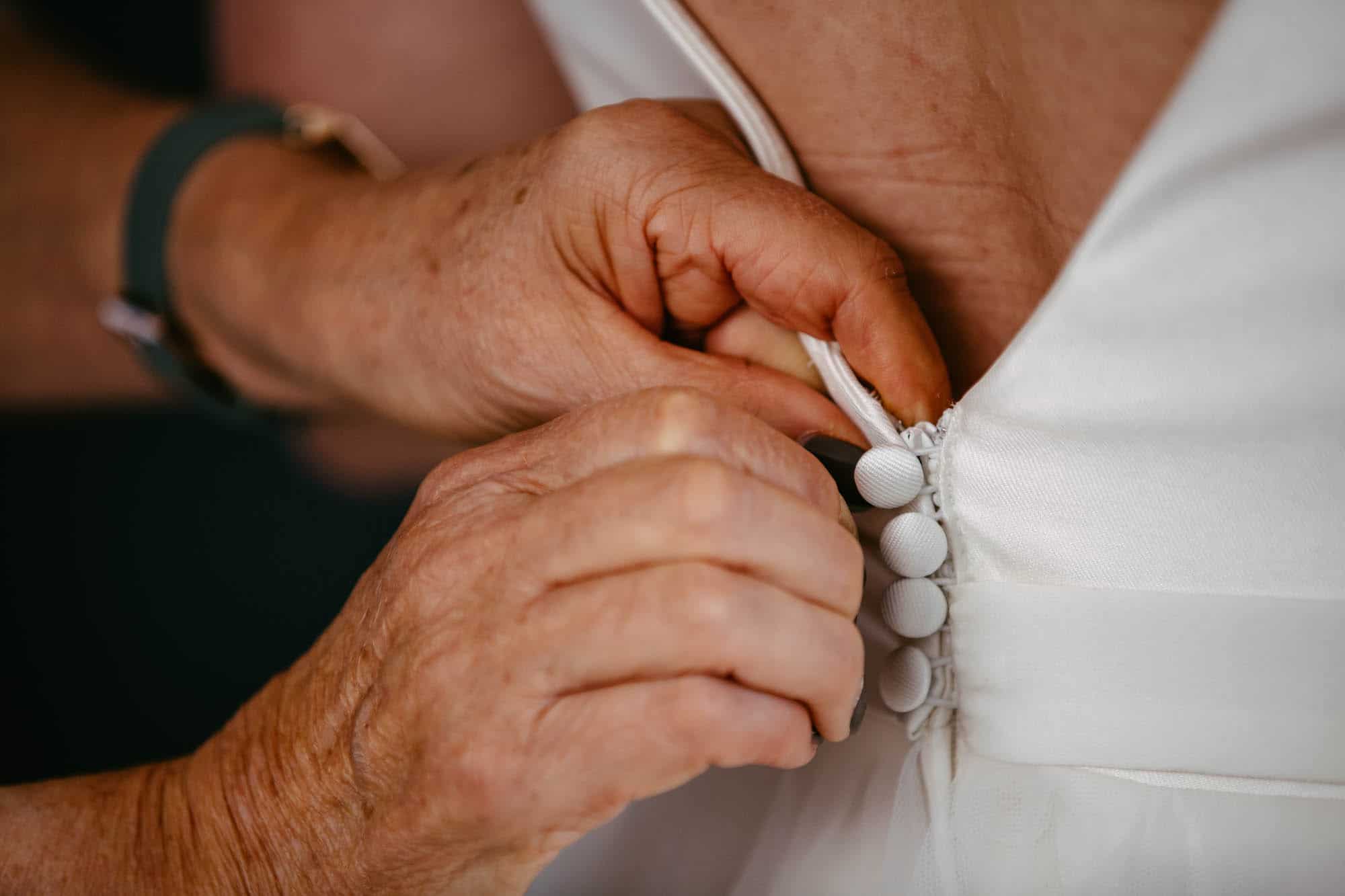 A woman puts a button on a bride's dress.