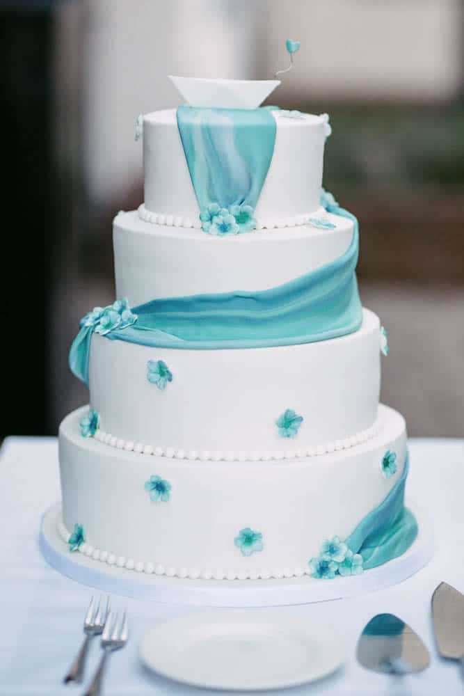 A white wedding cake with blue flowers on top, providing wedding inspiration.