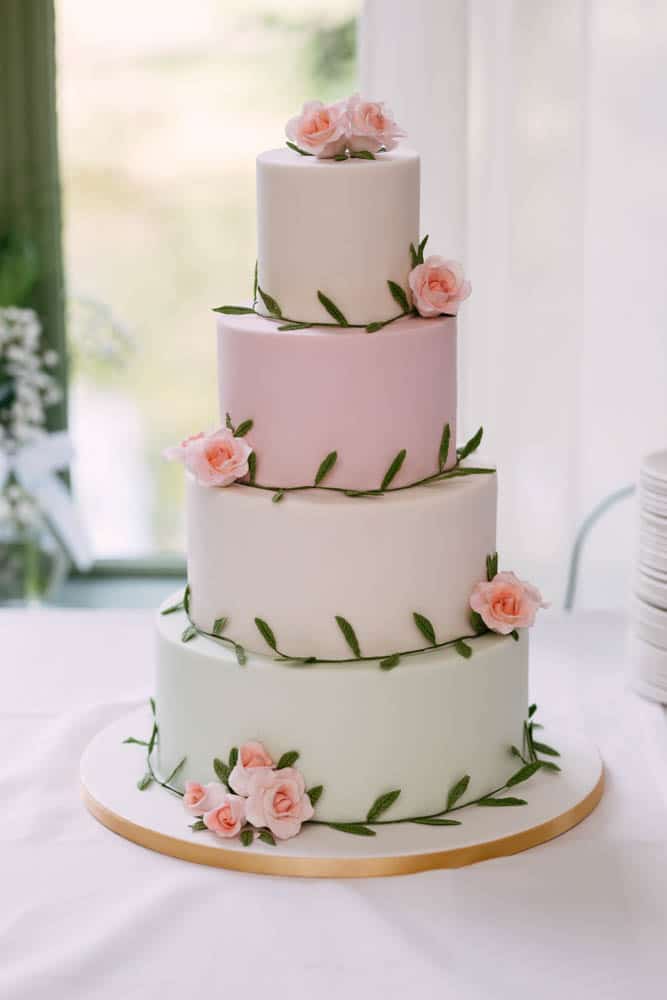 Een bruidstaart met drie lagen, versierd met roze en witte rozen, voor bruiloftsinspiratie.
