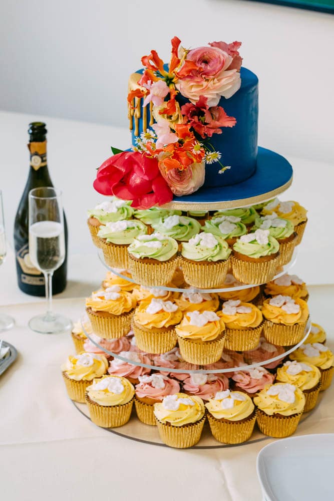 A three-tier cake with cupcakes embellished with wedding inspiration, accompanied by a bottle of wine.