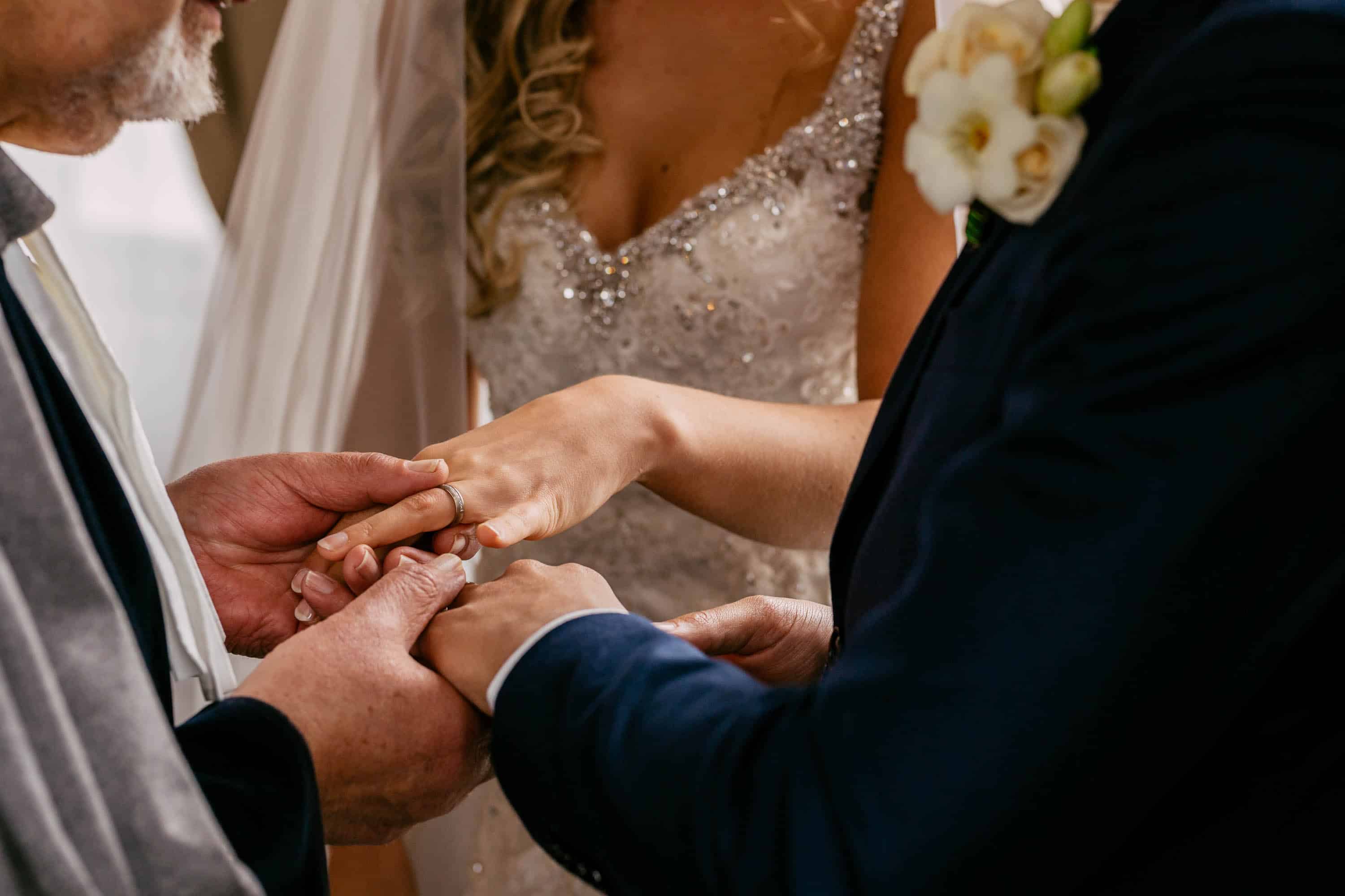 Een man doet een trouwring aan de vinger van een bruid.