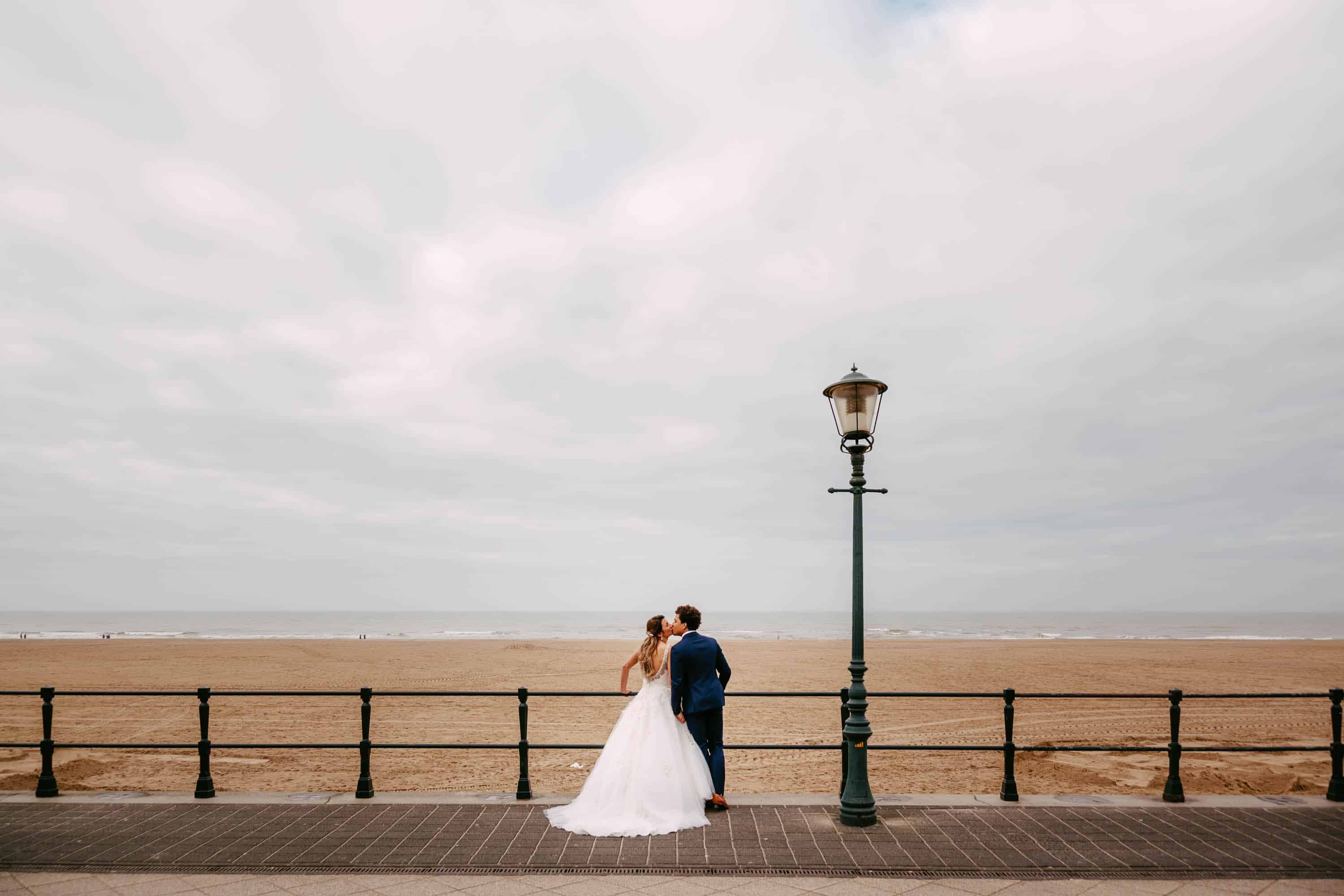 Een bruid en bruidegom staan bij een lantaarnpaal op het strand.