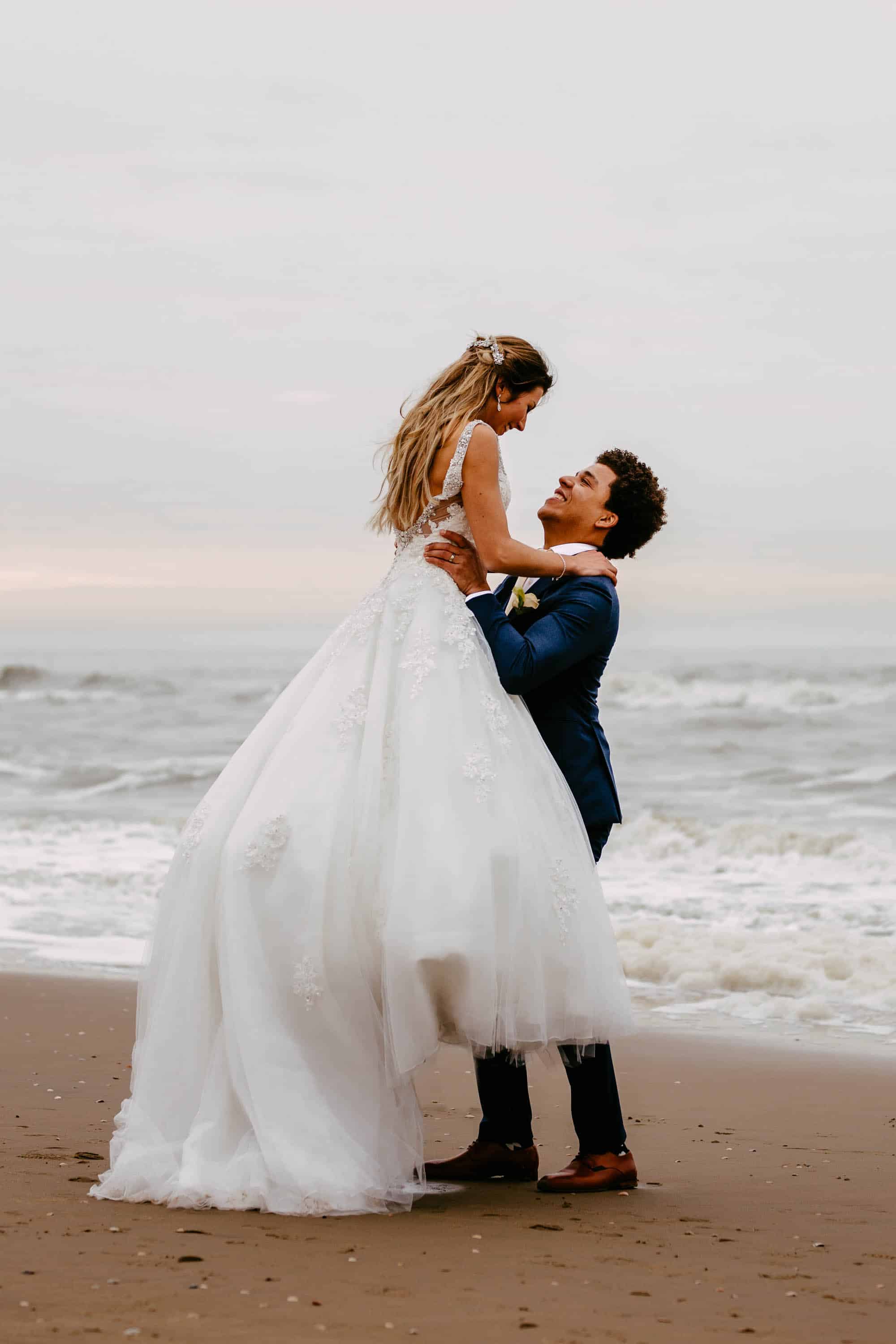 Een bruid en bruidegom knuffelen op het strand.