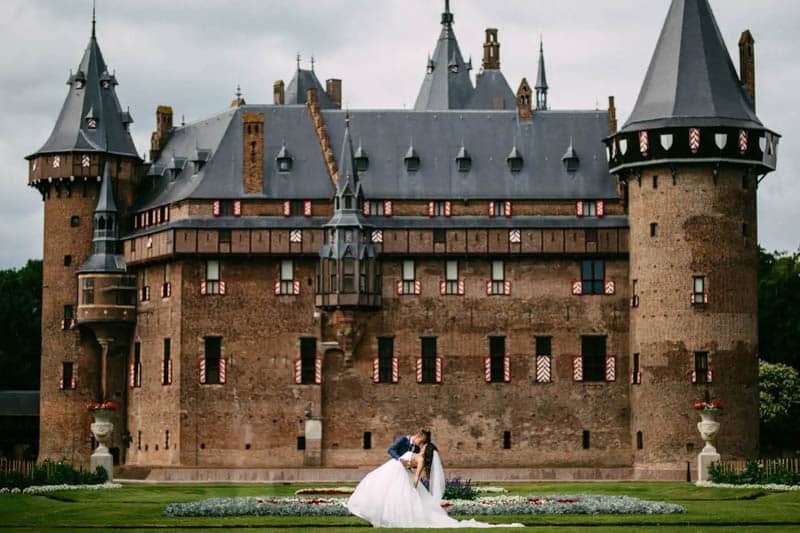 A couple pose in front of a beautiful castle on their wedding day.