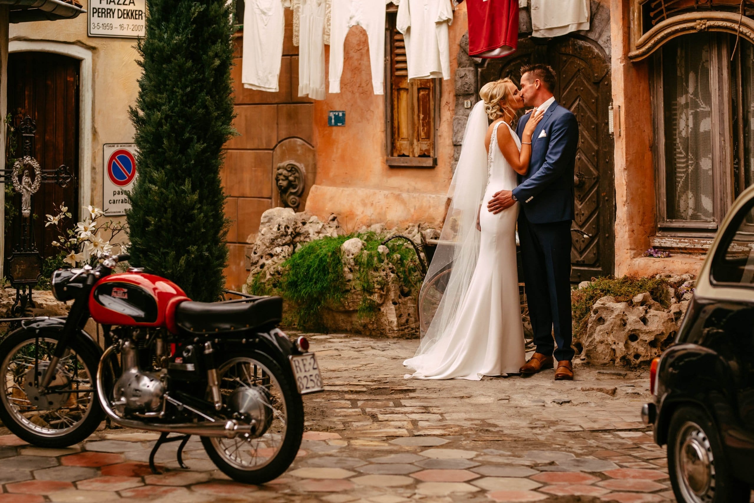 A bride and groom kiss in front of a motorbike.
