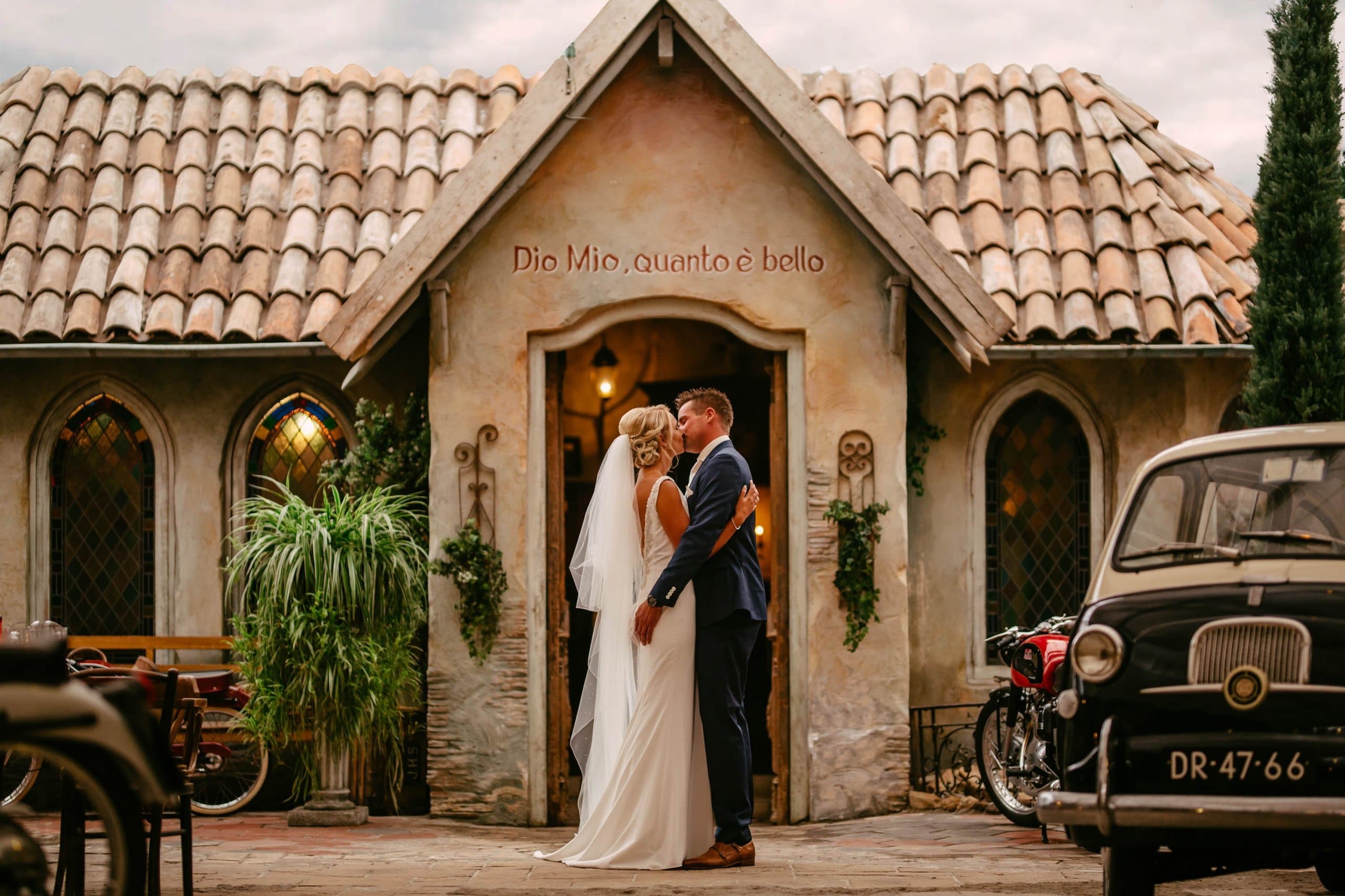 A bride and groom kiss in front of a restaurant.