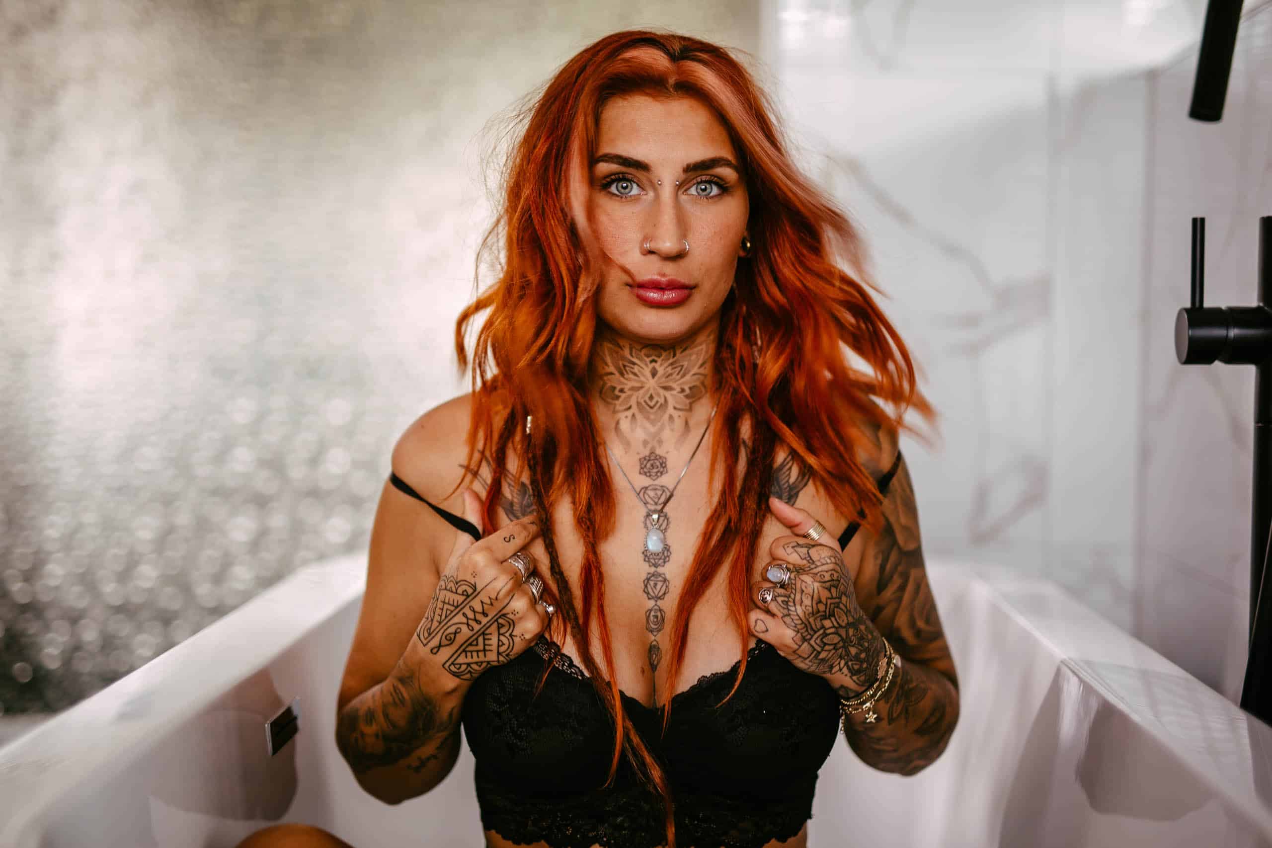 A woman with red hair during a boudoir shoot in Hoek van Holland, sitting in a bathtub decorated with tattoos.