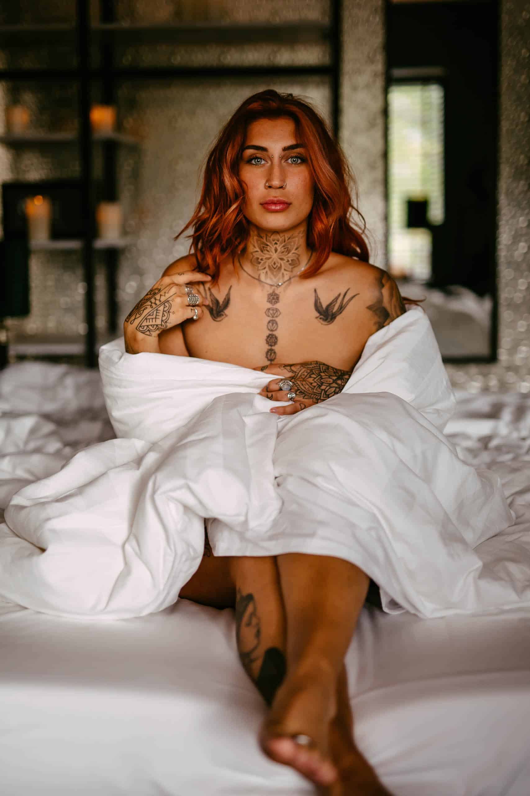 A woman with tattoos in a boudoir shoot in Hoek van Holland, posing seductively on a bed.