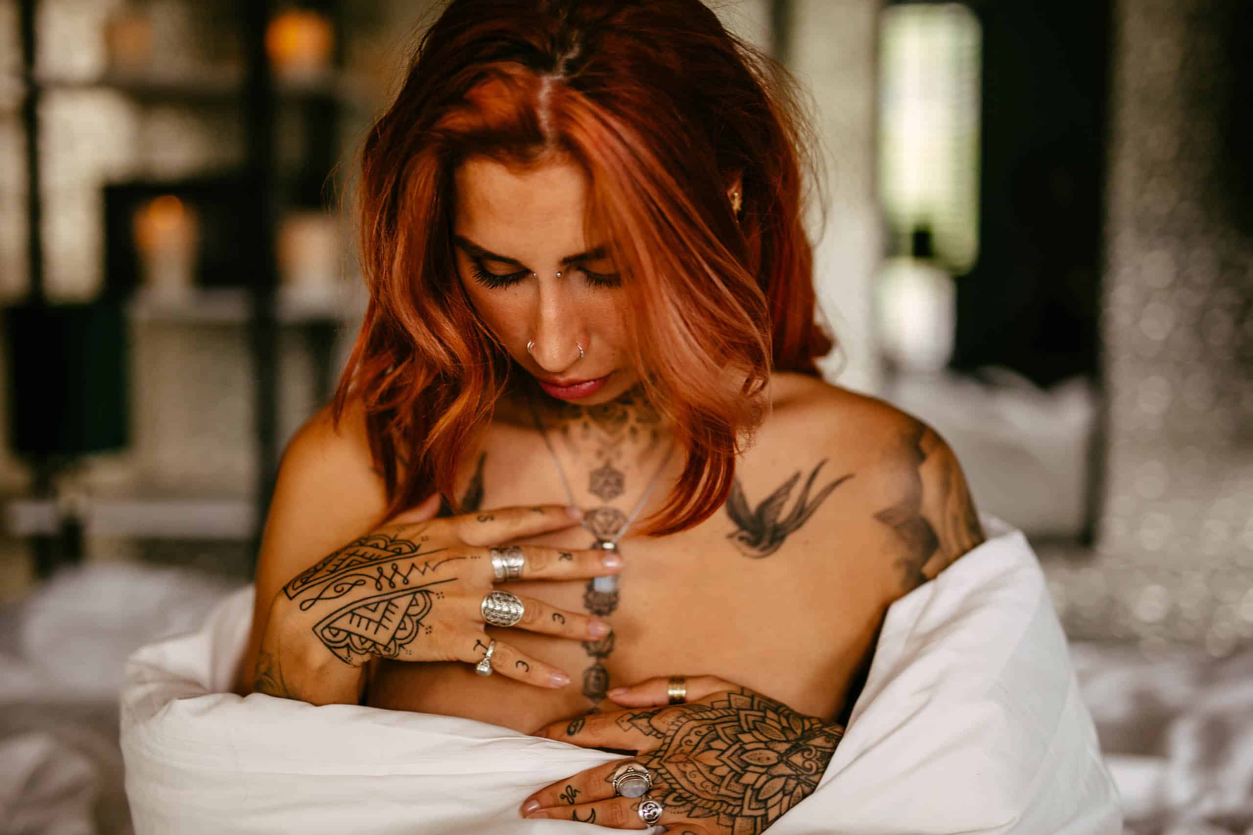 A woman with red hair and tattoos poses seductively during a boudoir shoot in Hoek van Holland.