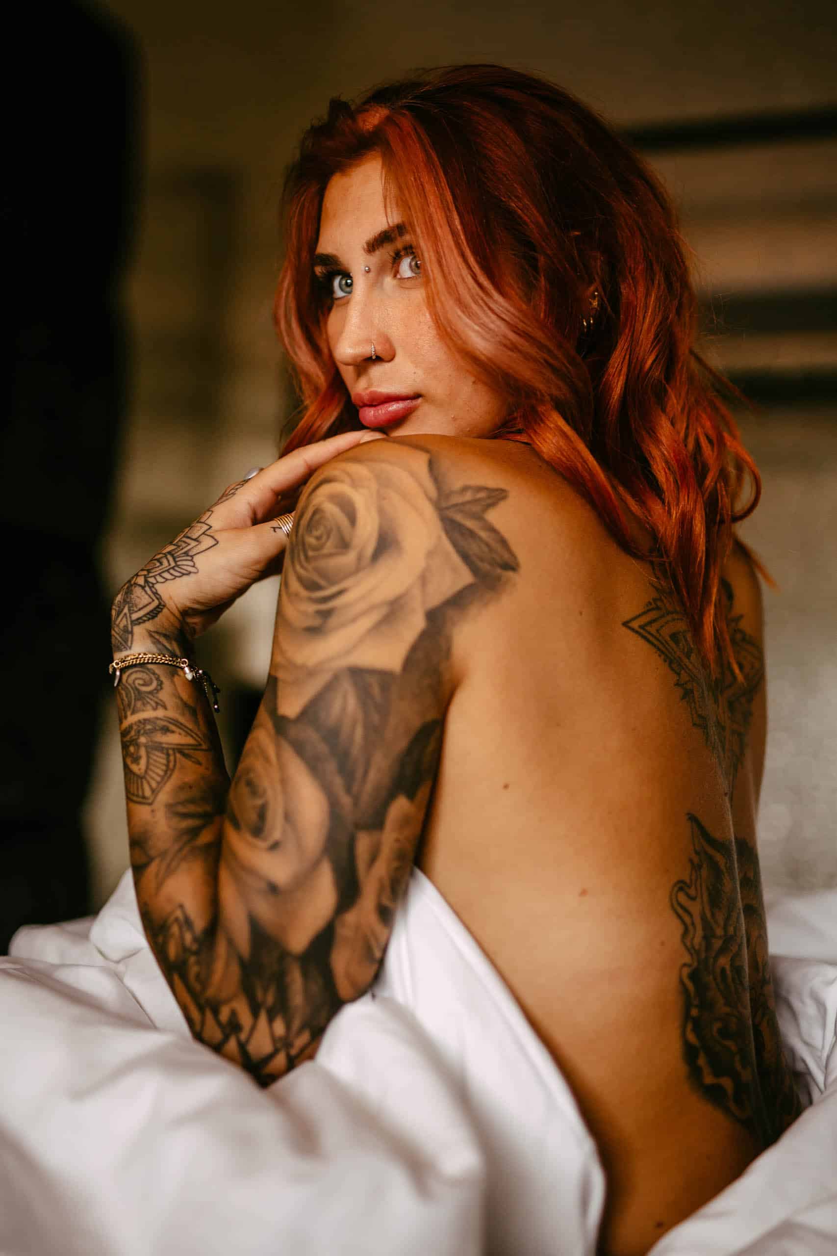 A woman with red hair and tattoos poses for a boudoir shoot in bed in Hoek van Holland.