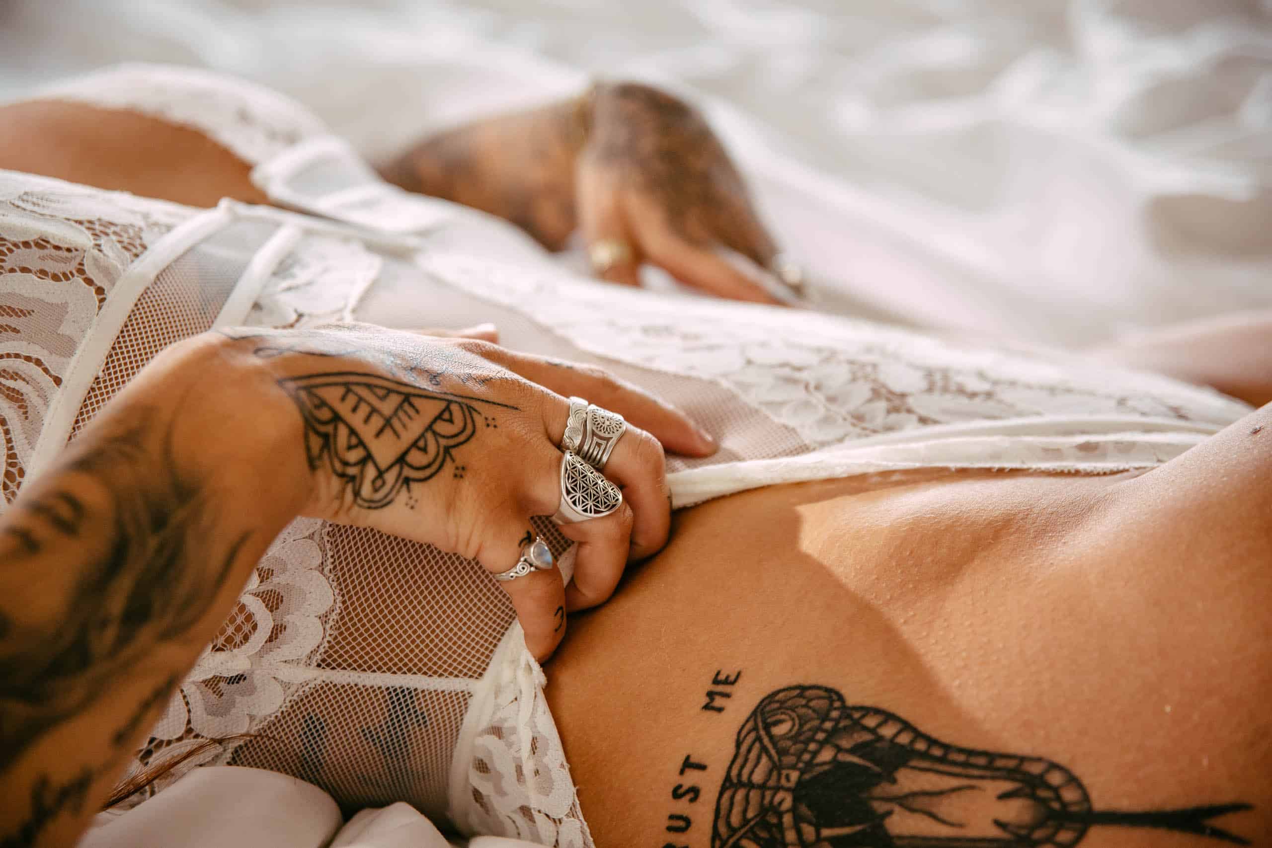 A woman with tattoos poses for a boudoir shoot on a bed in Hoek van Holland.