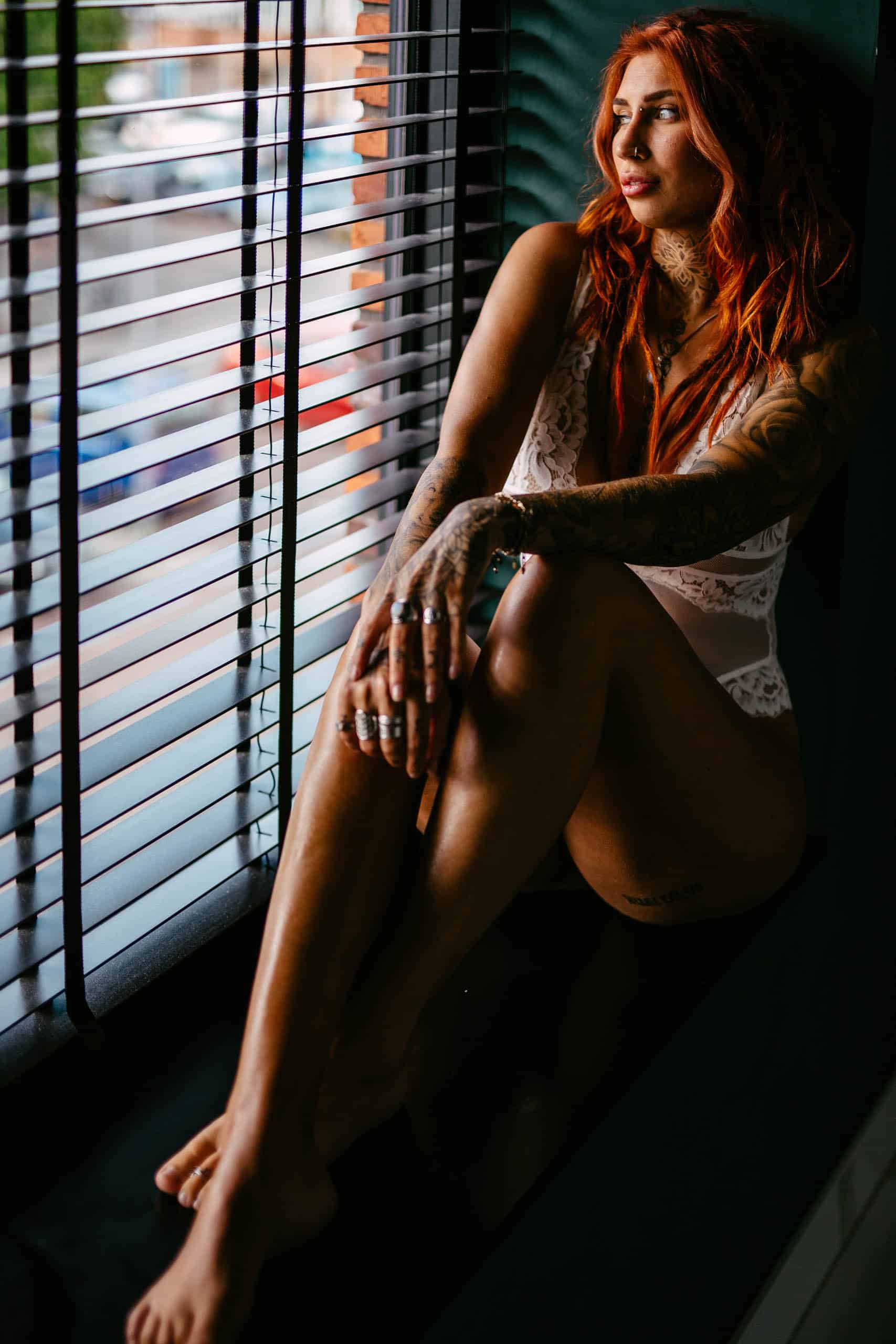 A woman with red hair sitting on a windowsill during a boudoir shoot in Hoek van Holland.
