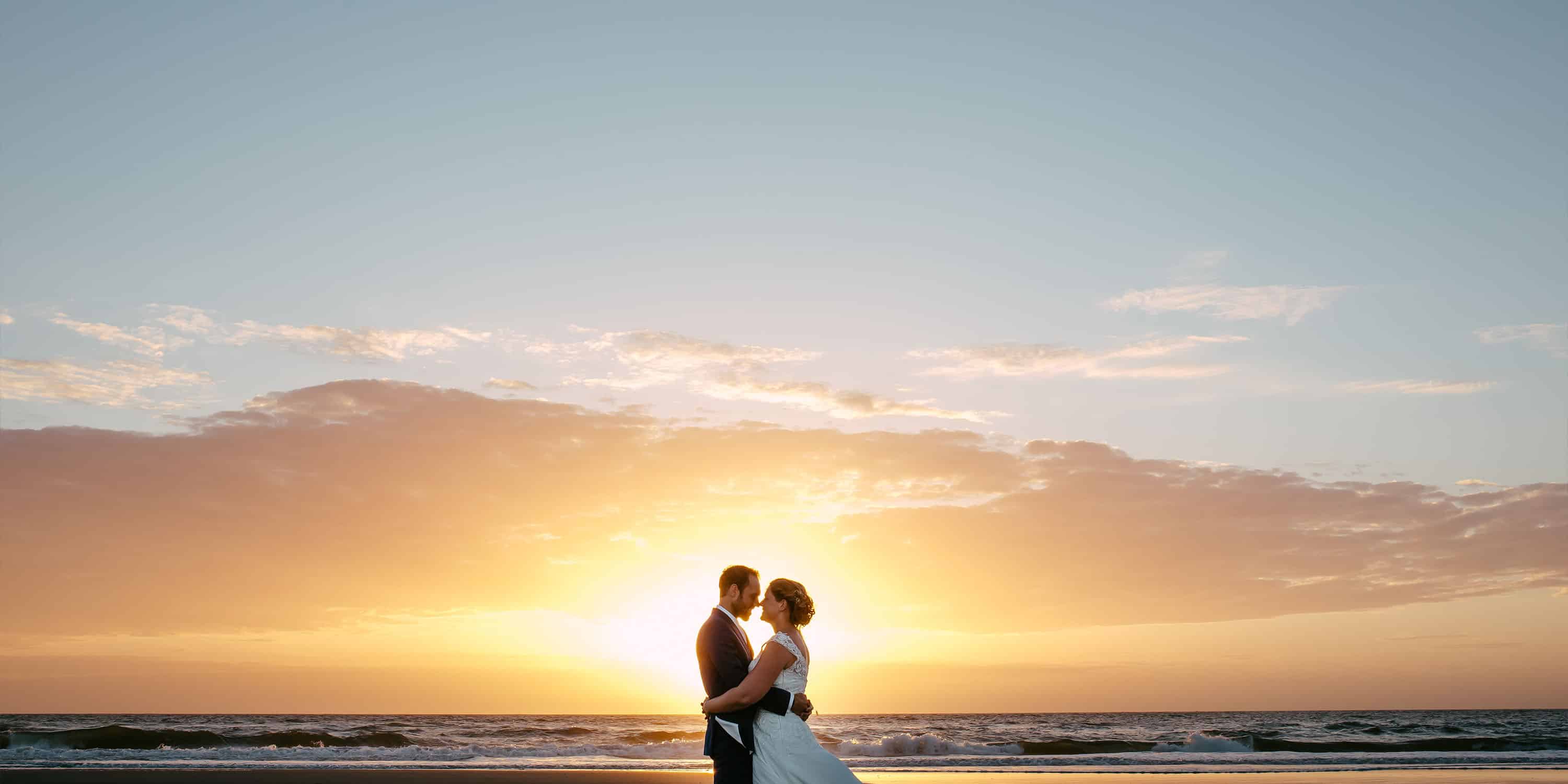 Een goedkoop trouwend bruidspaar staand op het strand bij zonsondergang.