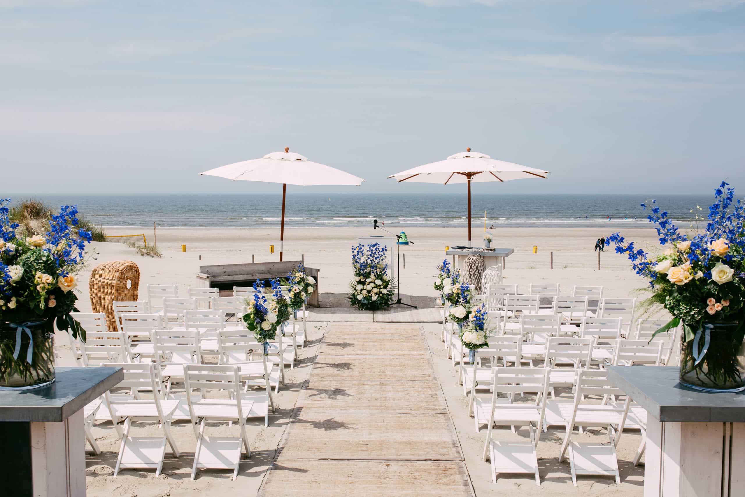 A wedding on the beach with chairs and umbrellas.