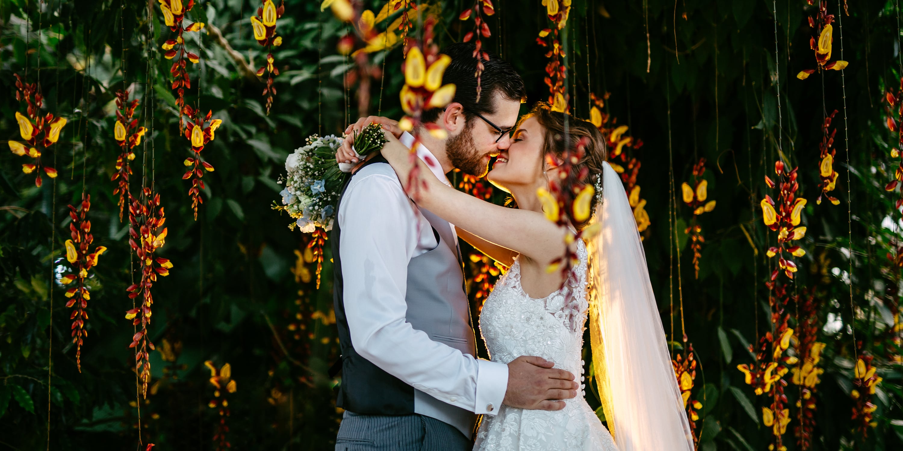Een bruid en bruidegom delen een romantische kus onder een prachtig bladerdak van bloemen op een van de pittoreske Fotolocaties in Zuid-Holland.