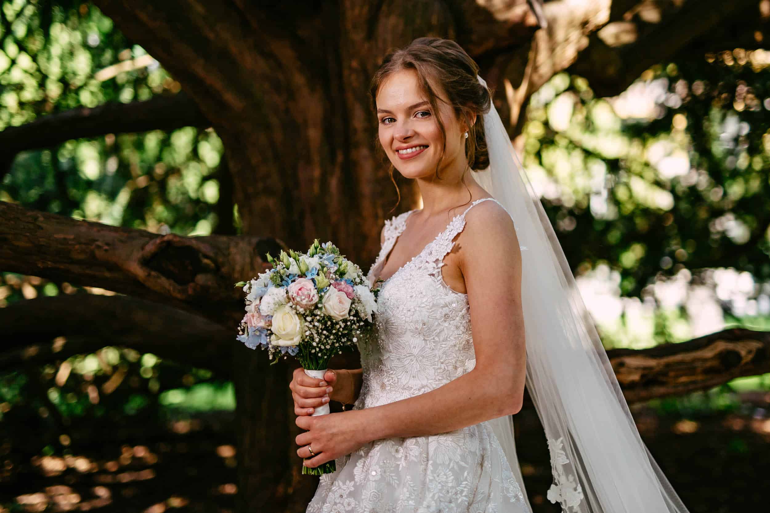 A bride with a bouquet in front of a tree at Wedding Botanical Garden Delft.