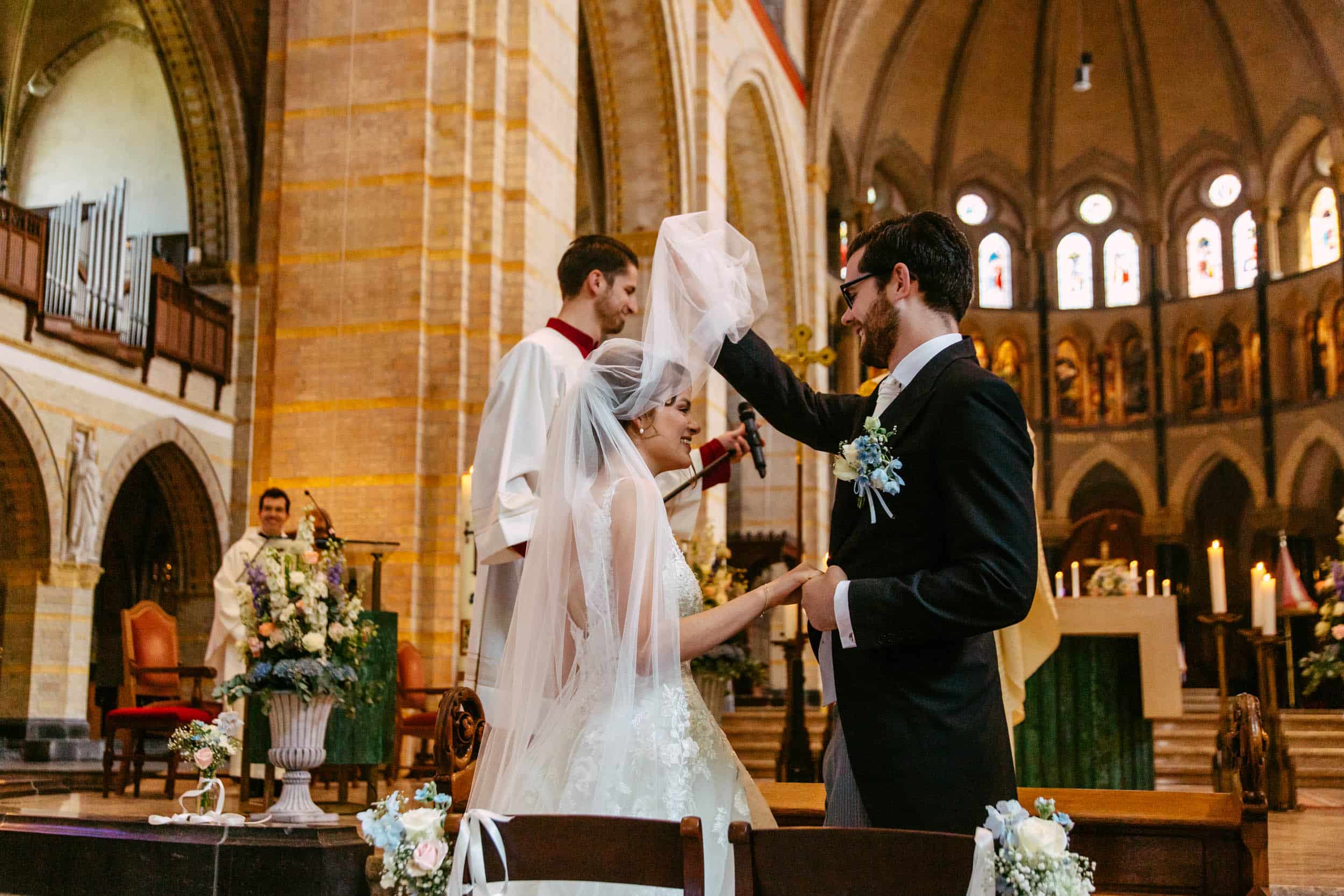 A bride and groom putting their veil on each other during their wedding in a church.