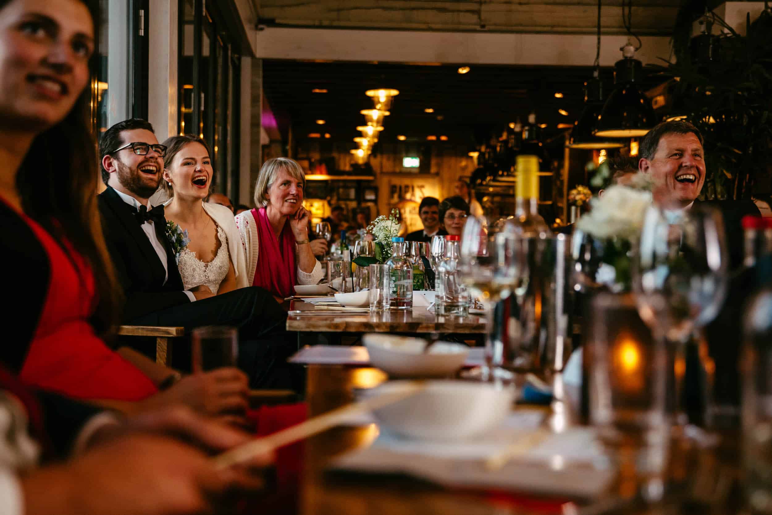 A group of people laughing at a restaurant table during a Wedding Ceremony at the Delft Botanical Garden.