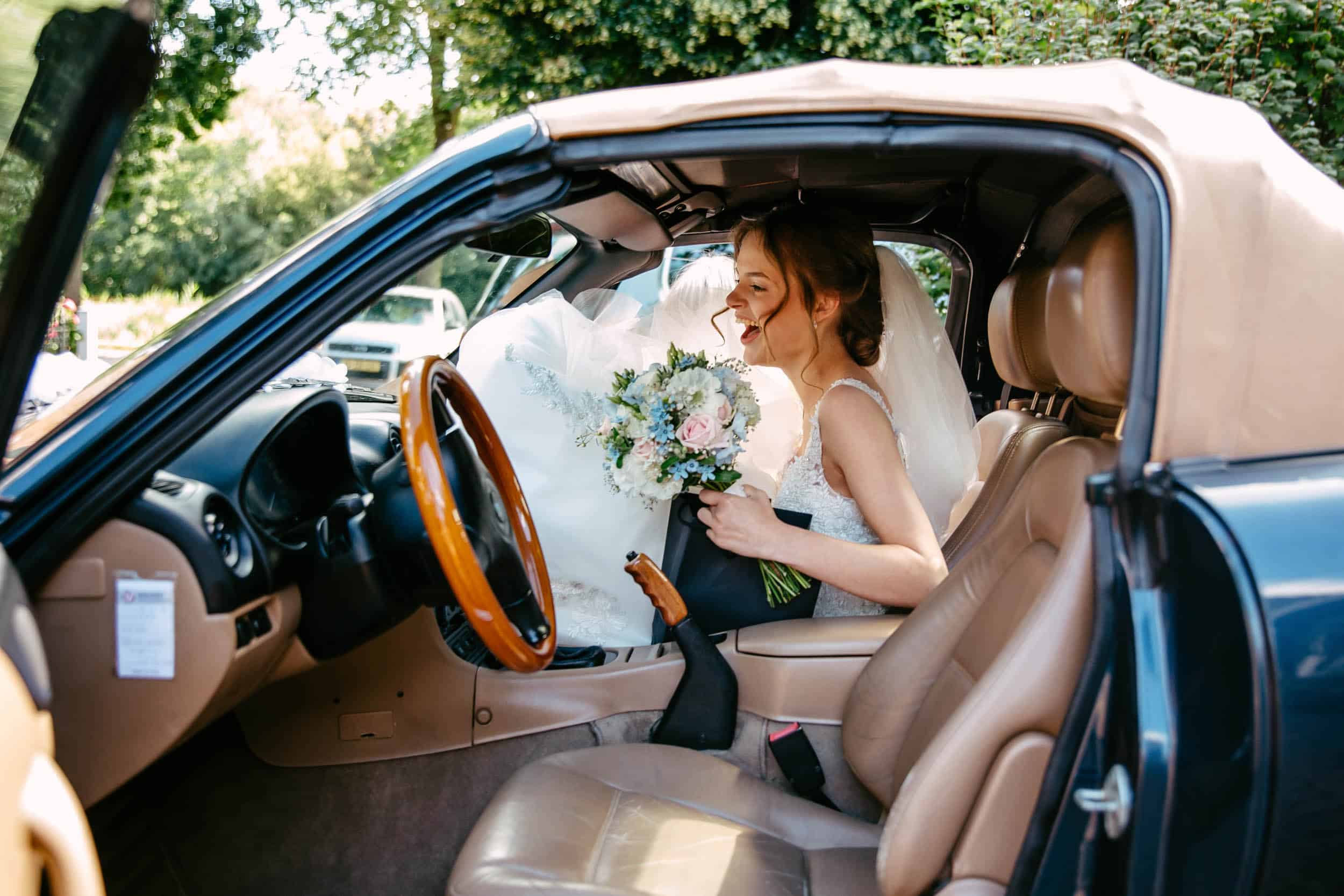 At Trouwerij Botanische Tuin Delft, a bride sits behind the wheel of a car.