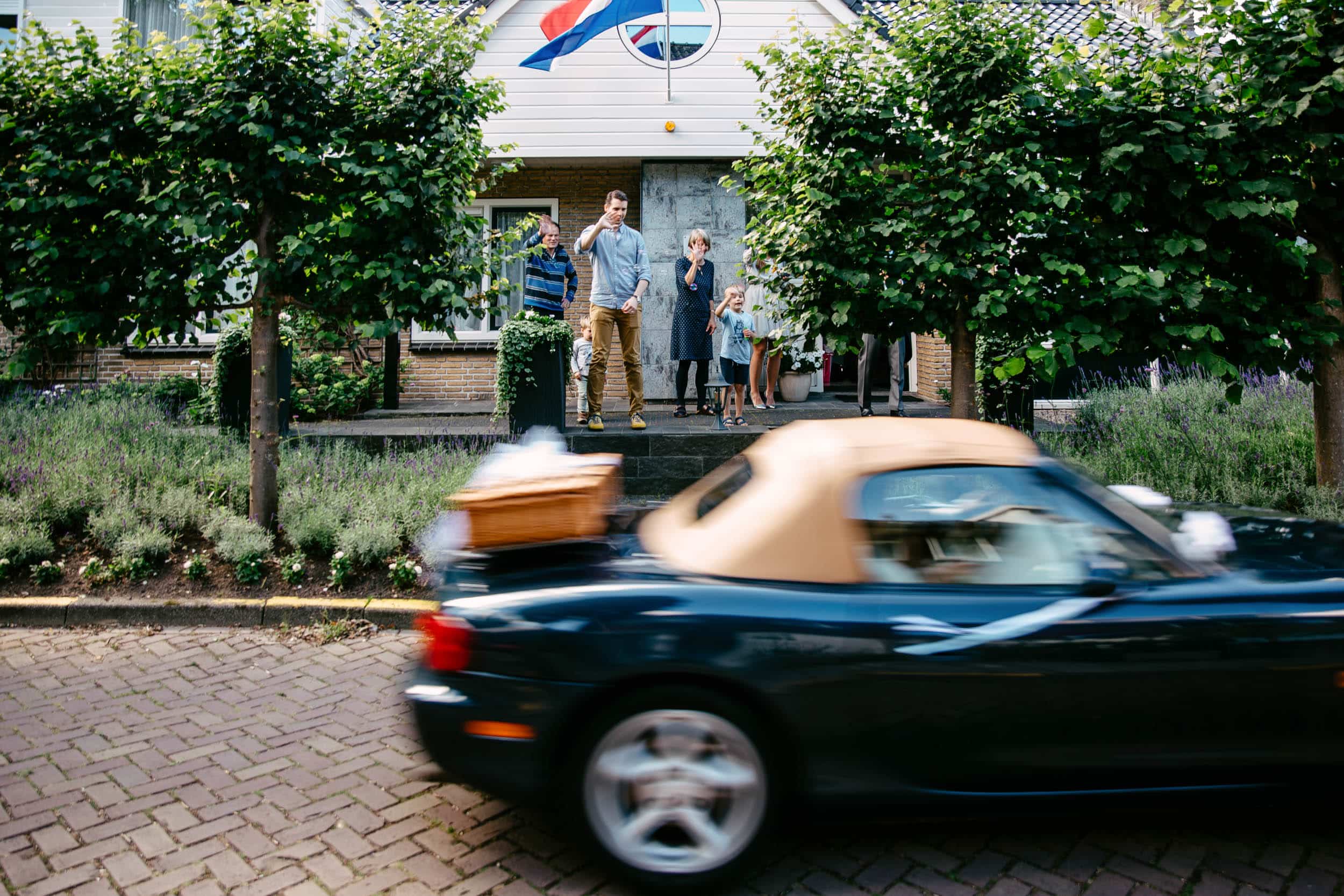 A family drives a sports car in front of a house of their Wedding.
