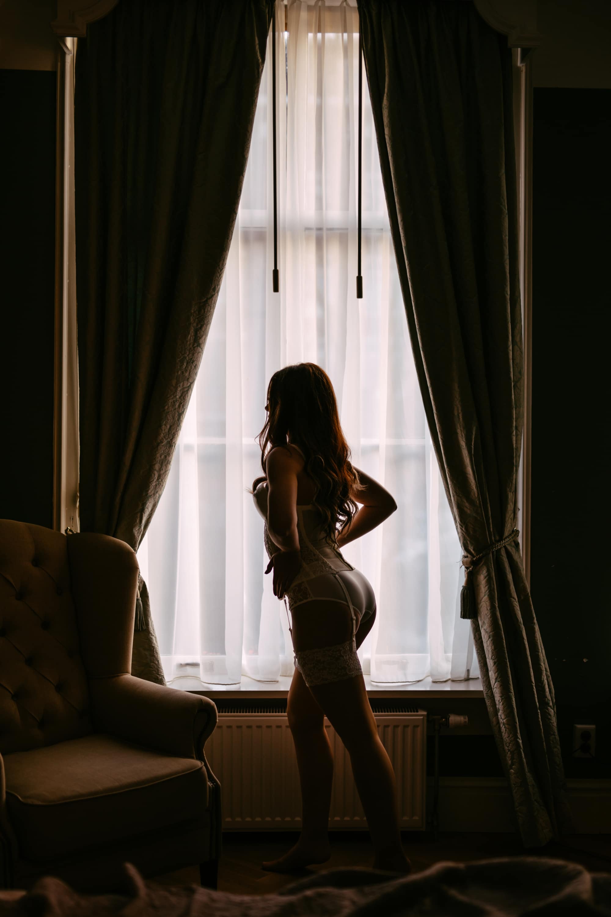 Een vrouw in lingerie staat voor een raam.